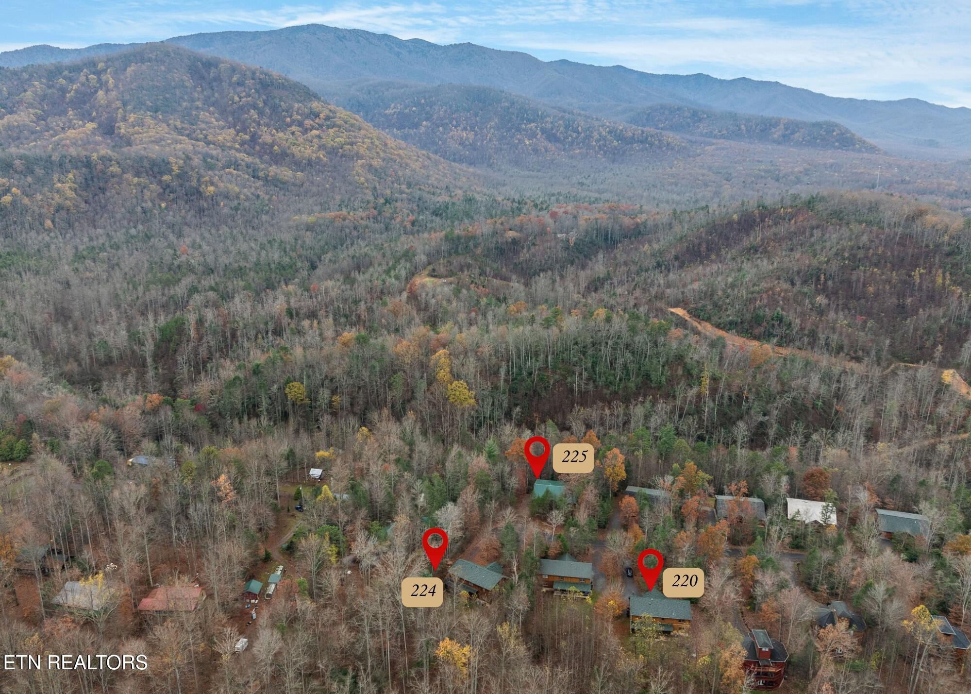 Aerial view of wooded cabins with mountain ridges beyond and map pins marking nearby properties.