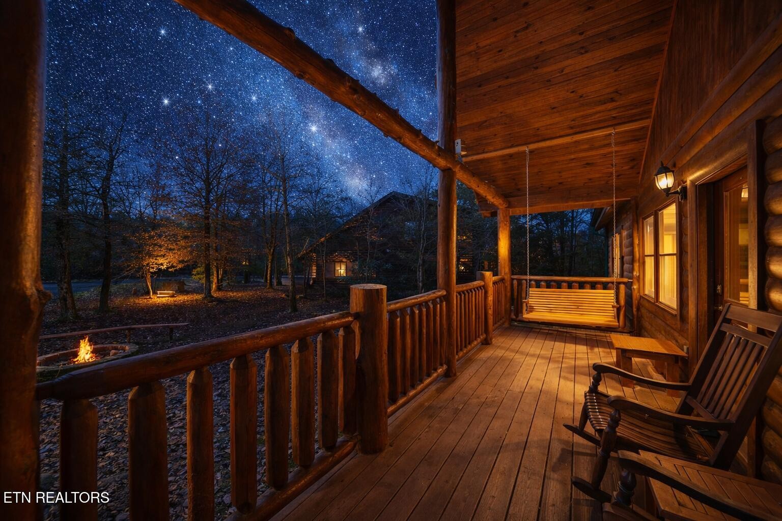 Covered cabin porch with rocking chairs and swing overlooking a fire pit beneath a starry sky.