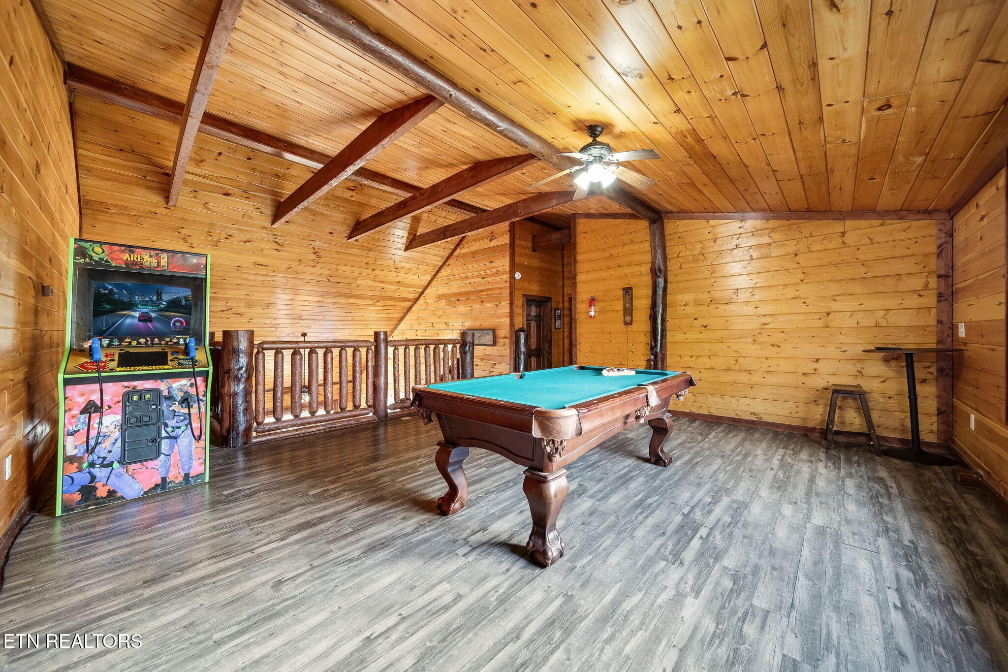 Wood-paneled game room with a pool table, arcade cabinet, and exposed ceiling beams.