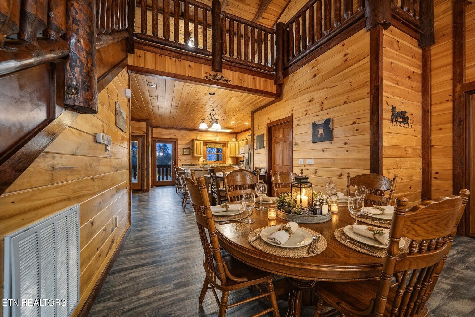 Cabin dining room with a set oval table, pine walls, rustic beams, and an open loft railing.