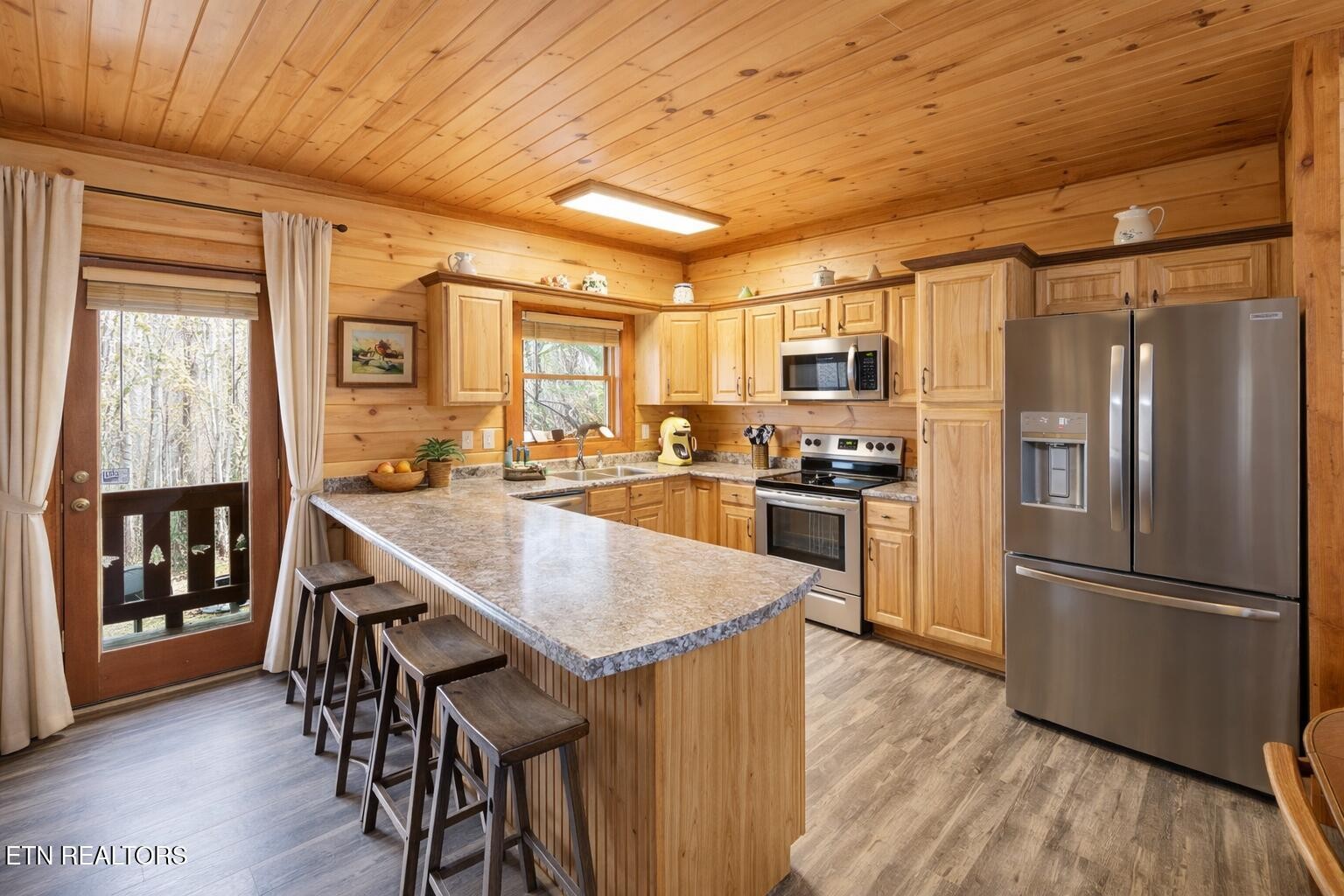 Wood-paneled kitchen with a large island, bar stools and stainless steel appliances.