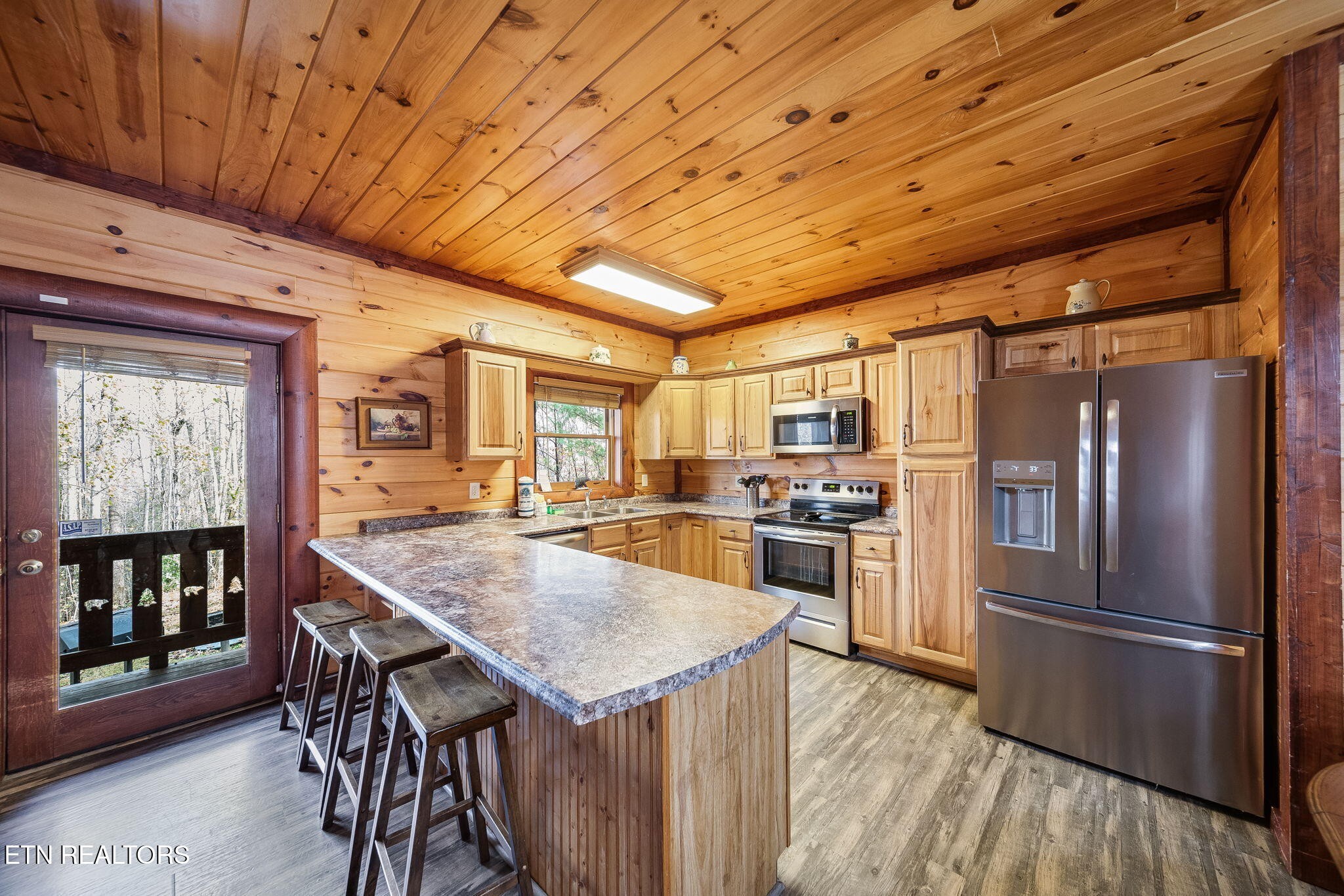 Cabin kitchen with knotty wood walls, stainless steel appliances, and a large breakfast bar.