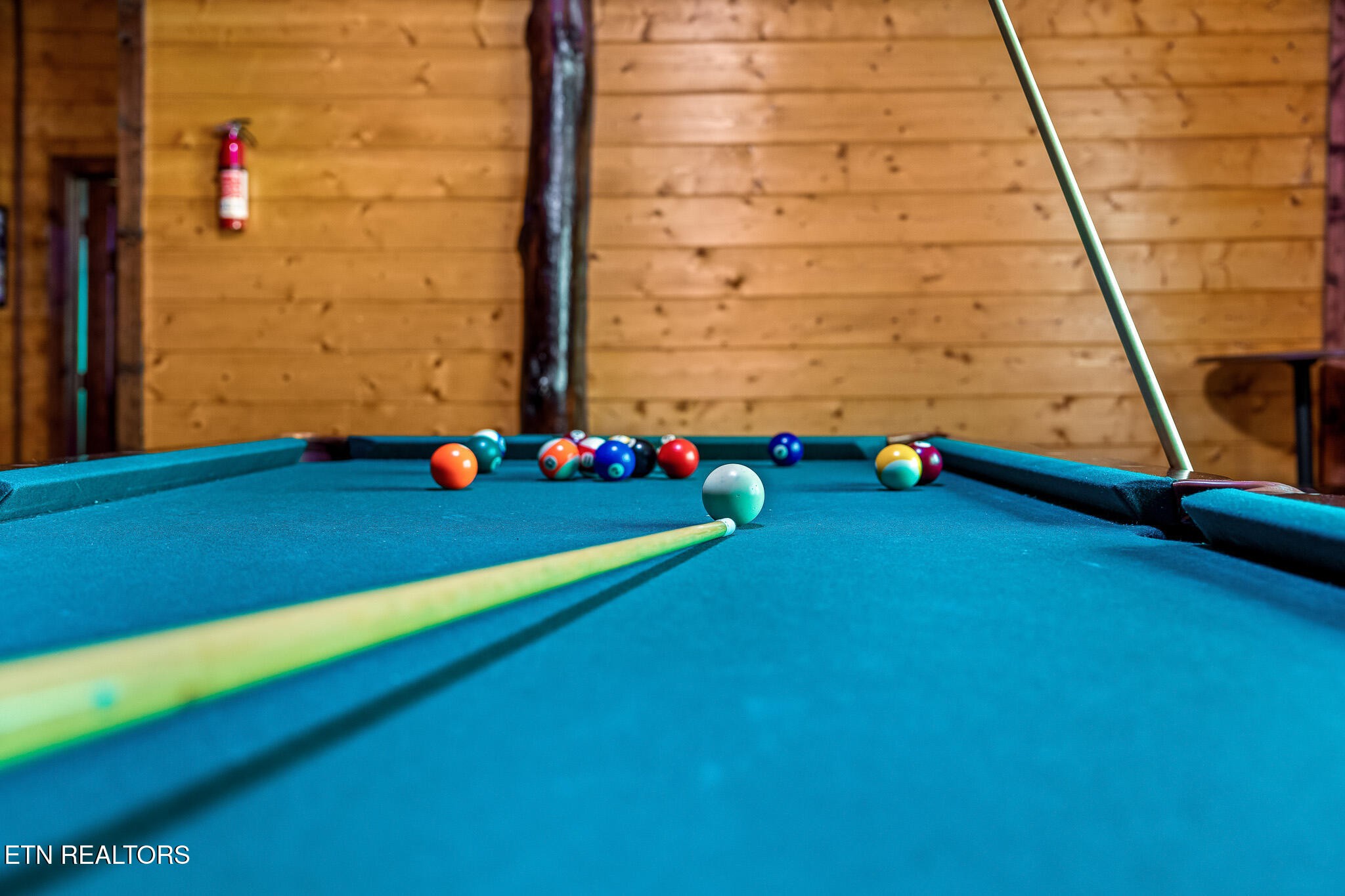 Blue-felt pool table with colorful balls and a cue in a wood-paneled game room.