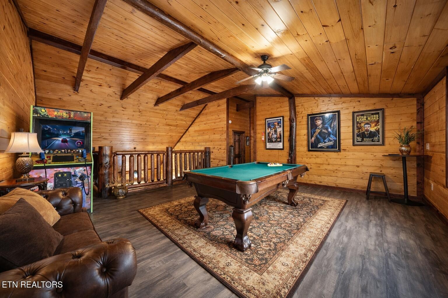Wood-paneled game room with a pool table, arcade game, and leather sofa.