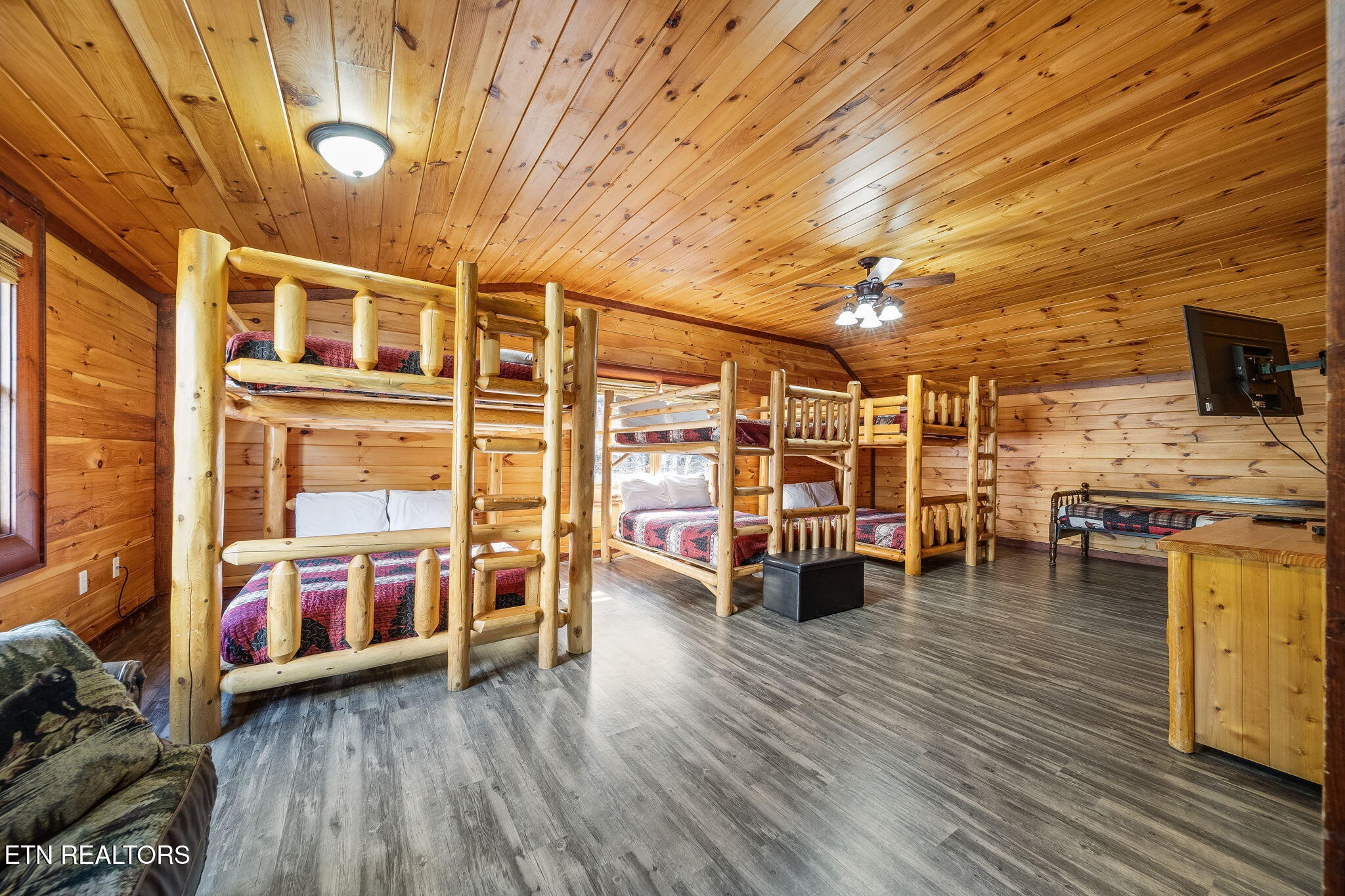 Cabin bunkroom with multiple rustic log bunk beds and warm wood-paneled walls and ceiling.