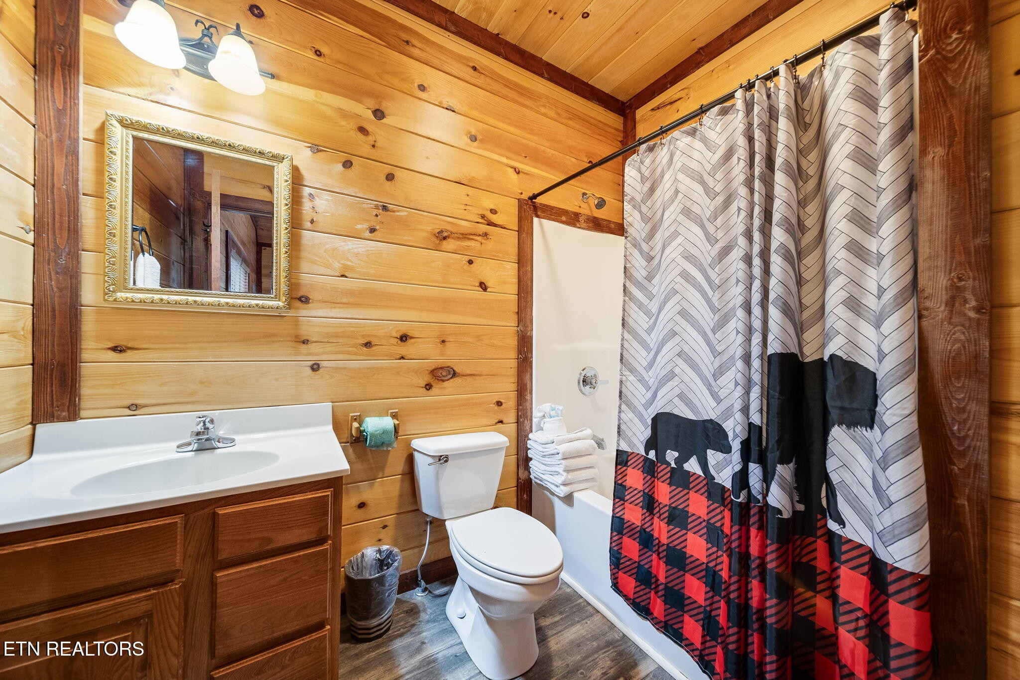 Bathroom with wood-paneled walls, a wooden vanity, and a gray, black, and red shower curtain.