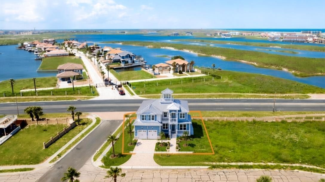 Blue two-story coastal home with an orange lot outline, grassy yard, and waterways nearby.