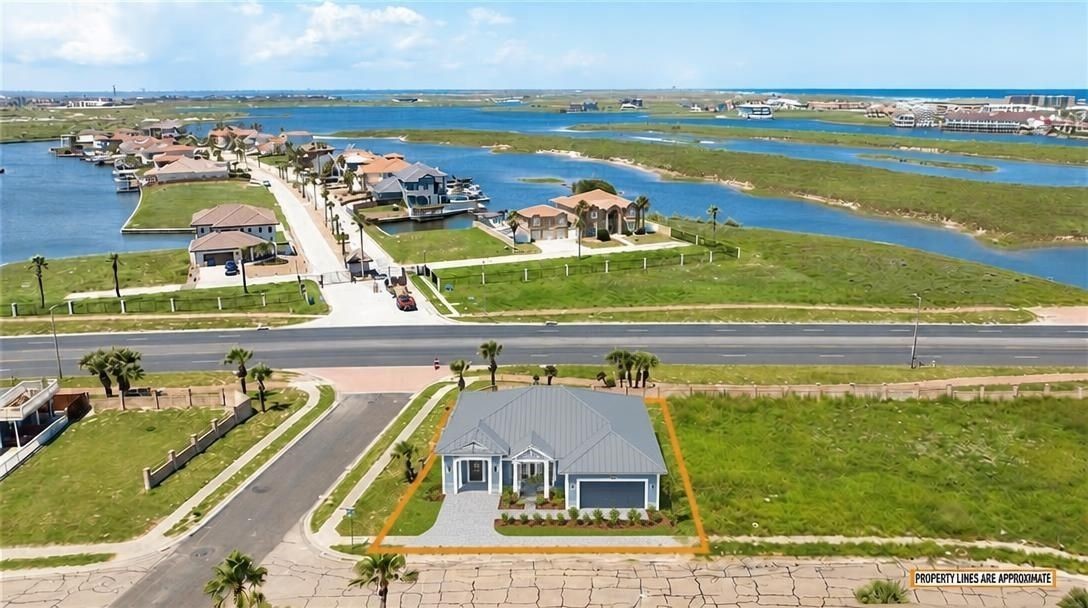 Aerial view of a gray-roofed home on a coastal lot, with waterways and marshland beyond.