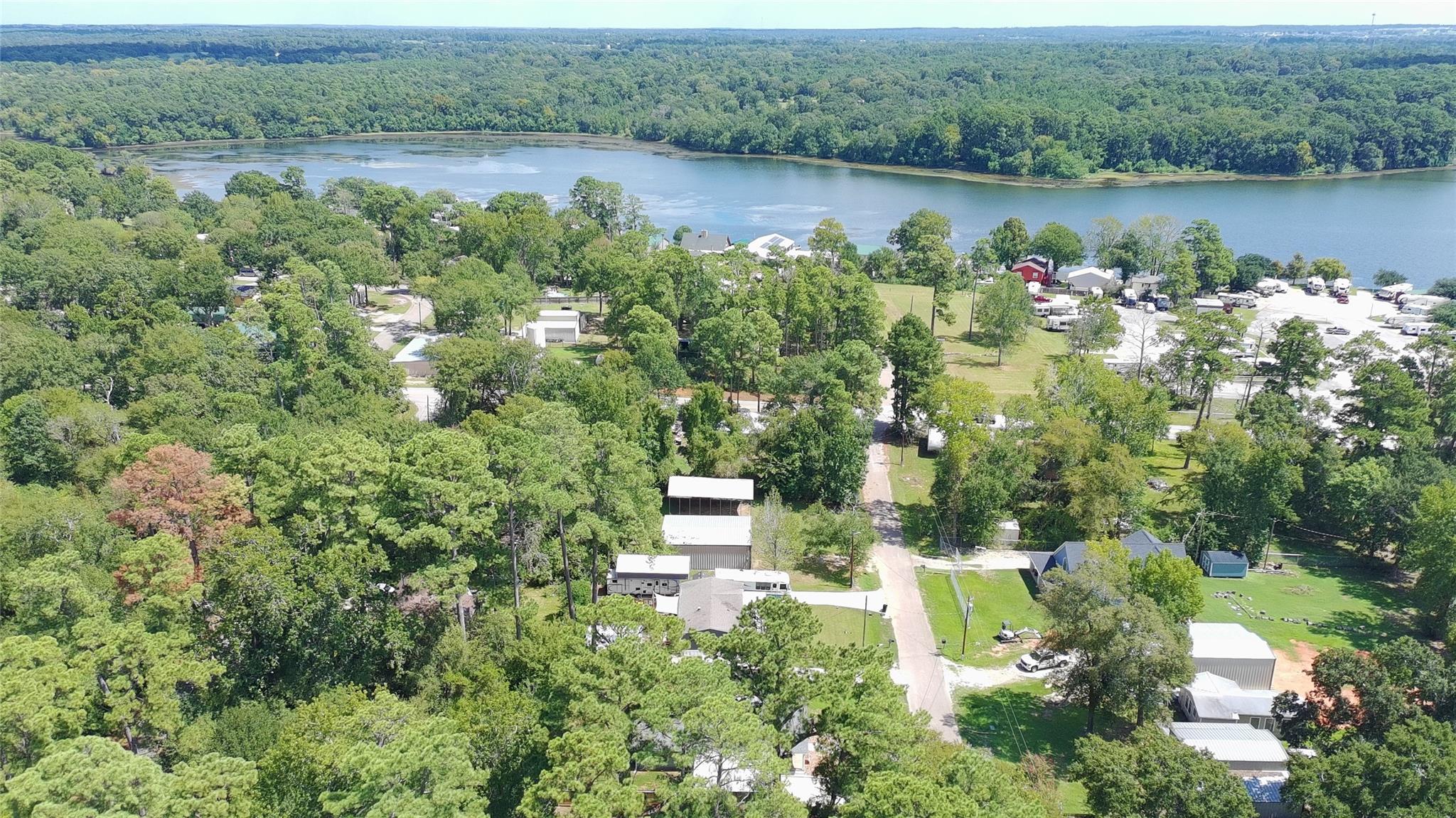 Aerial view of wooded lakeside homes and outbuildings, with a road and RVs along the shore.