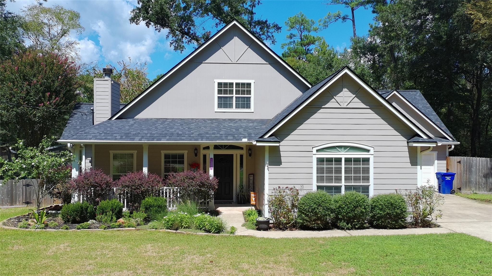 Gray gabled house with a covered porch, landscaped shrubs, and a broad front lawn.