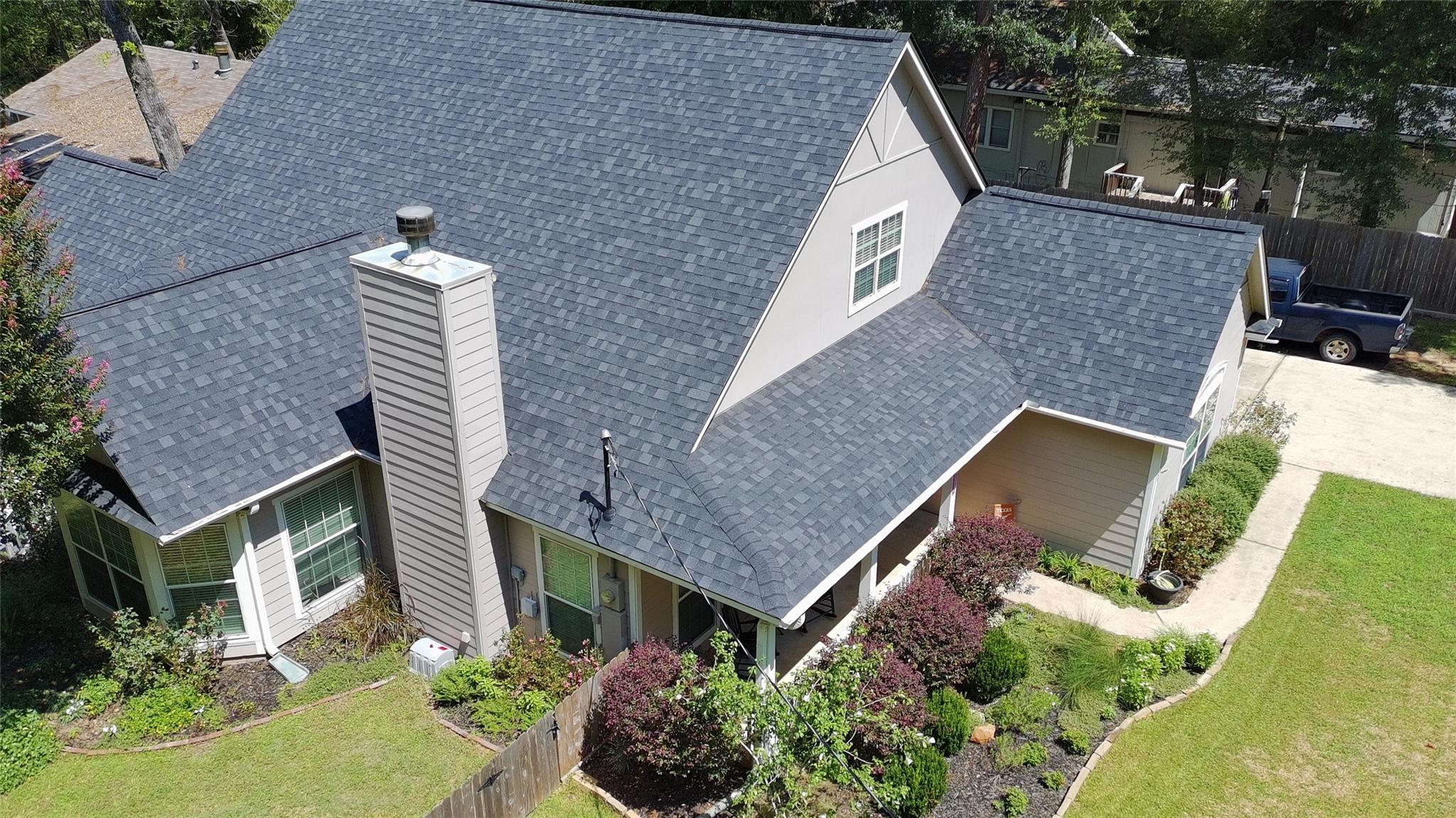 Aerial view of a gray-roofed two-story house with a chimney and landscaped yard.