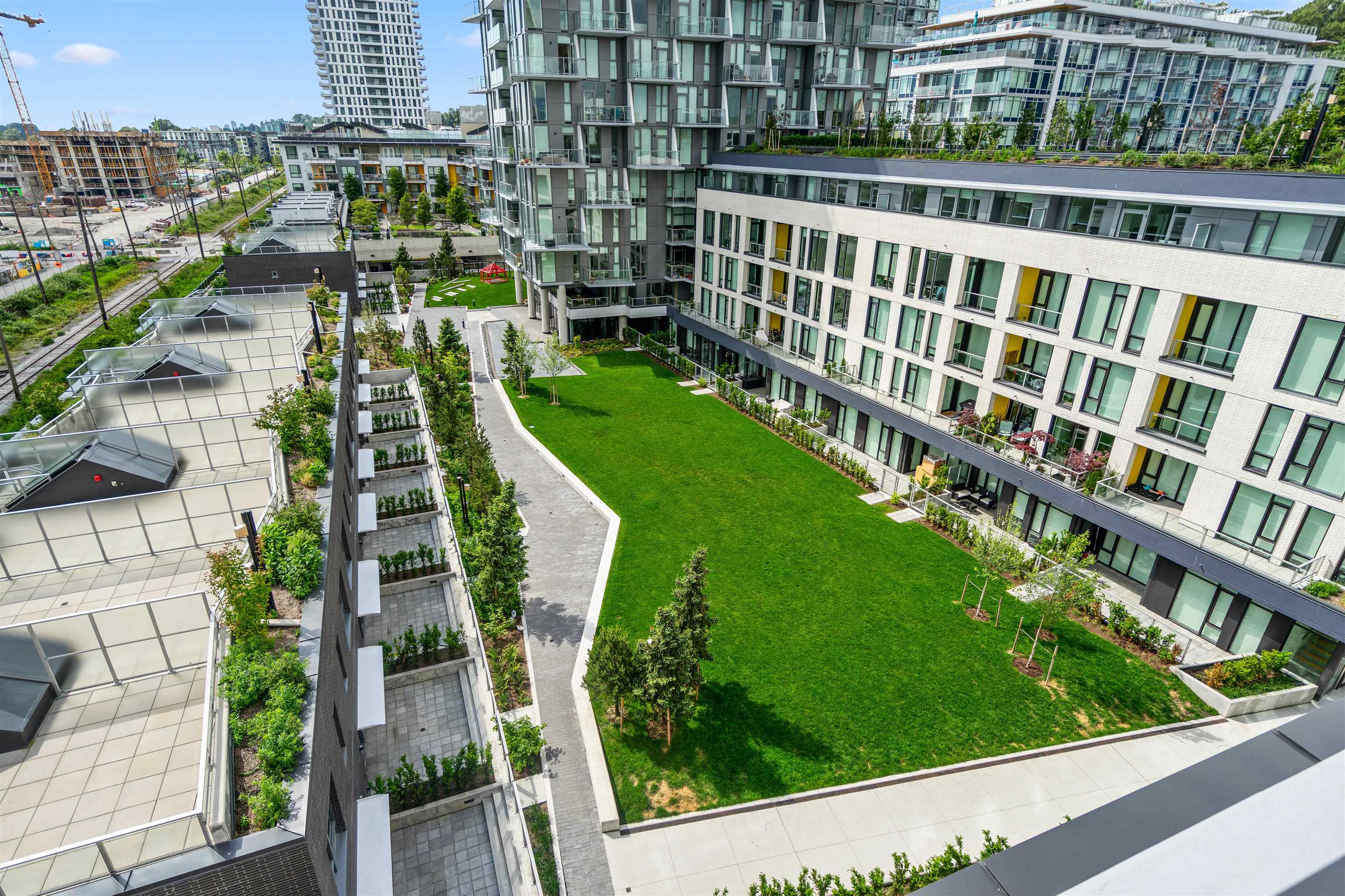 Condominium courtyard with a large green lawn, winding paths, landscaped terraces, and surrounding balconies.