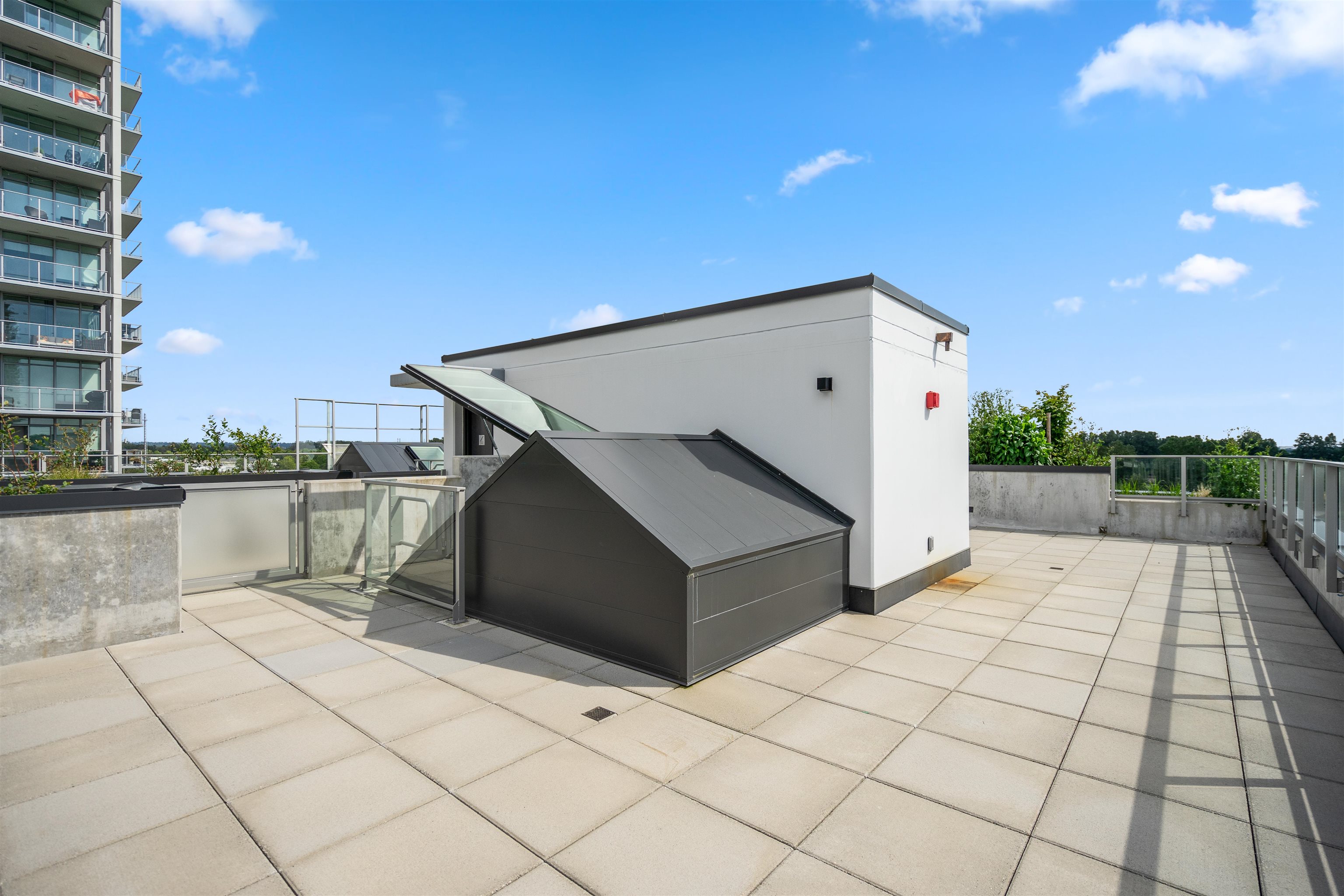 Condominium rooftop terrace with tiled paving, glass railings, and rooftop access structures.