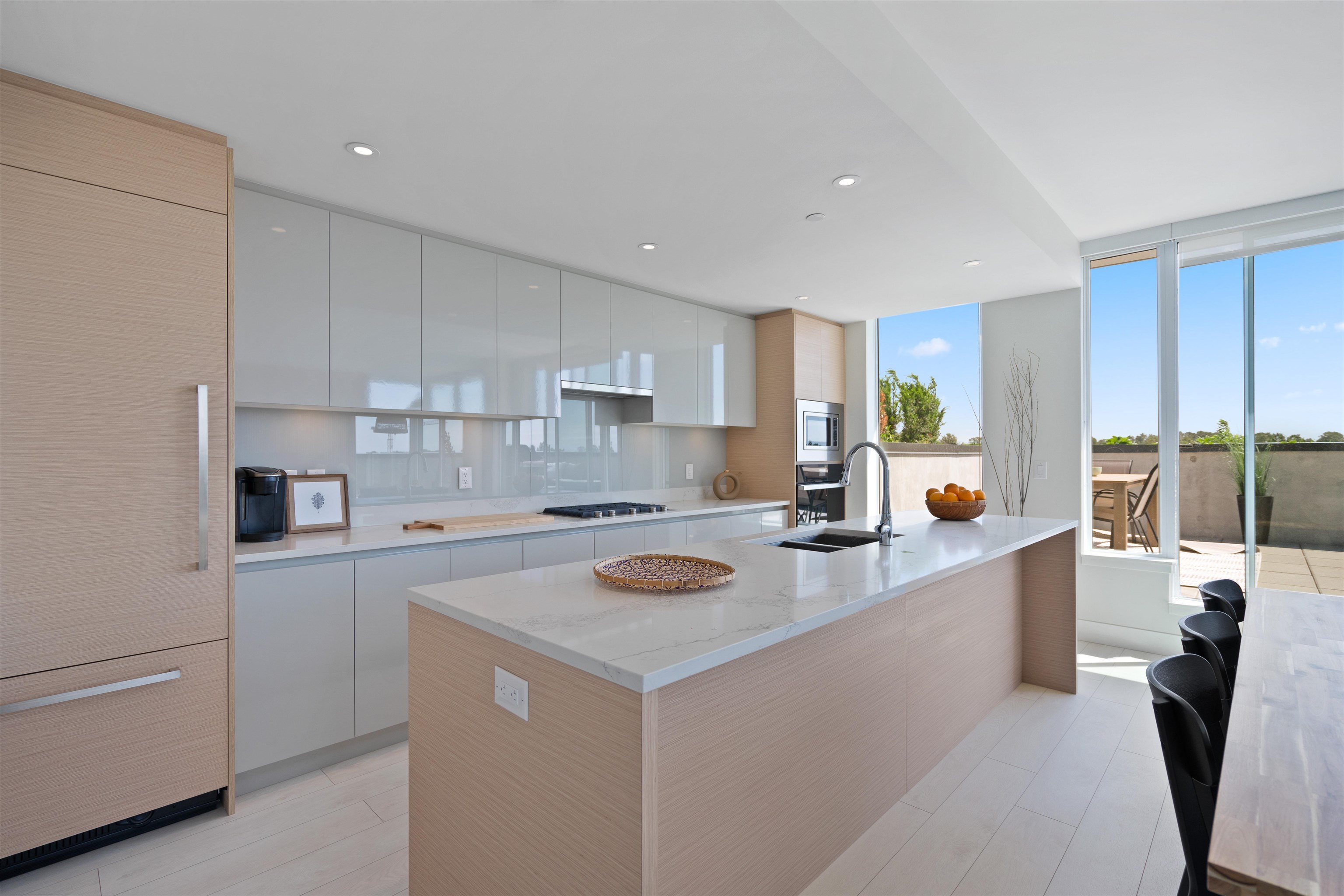 Modern kitchen with a large island, glossy white cabinets, and windows opening onto a terrace.