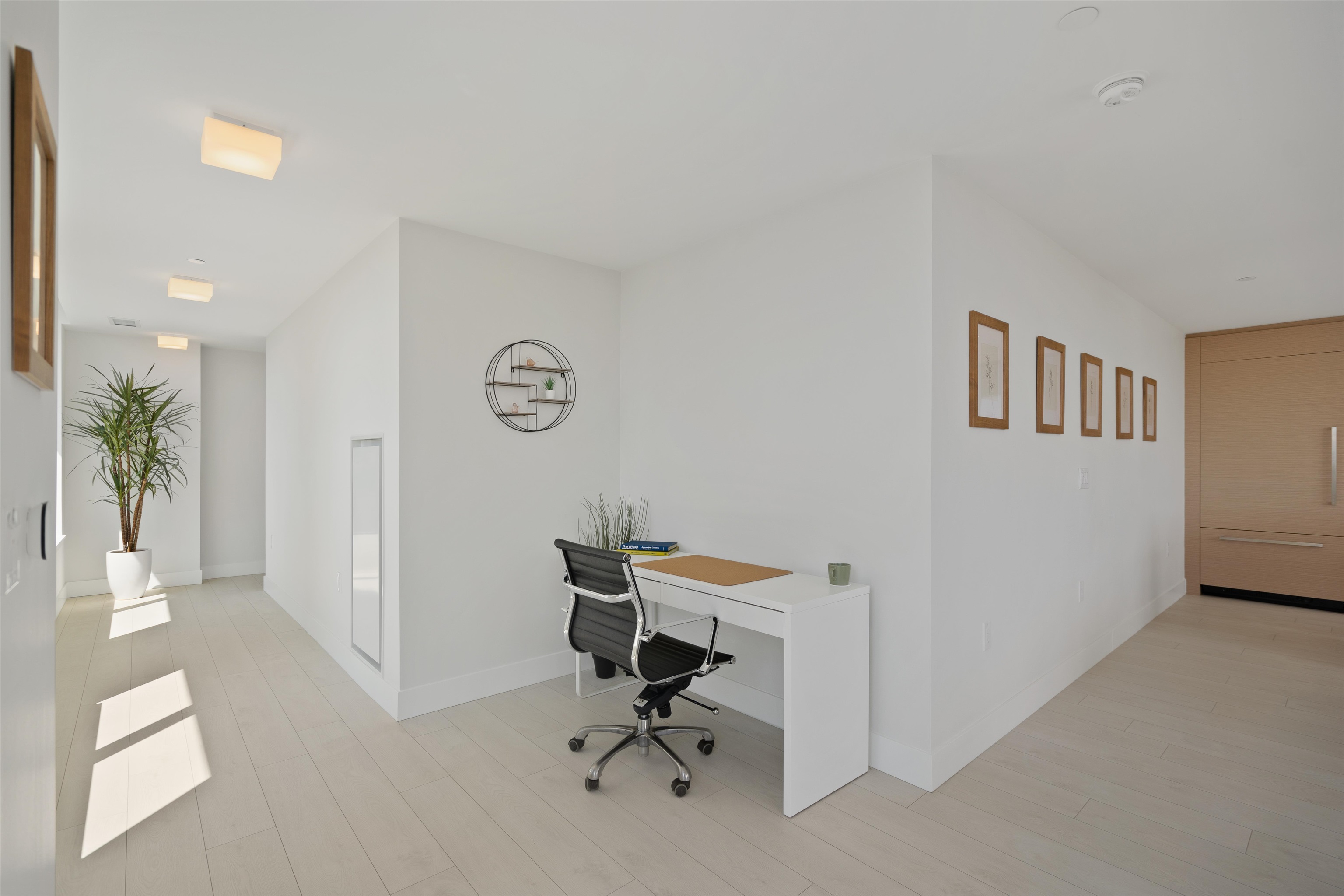 Bright condo entry hall with a compact desk, black office chair, potted plant, and wood entry door.