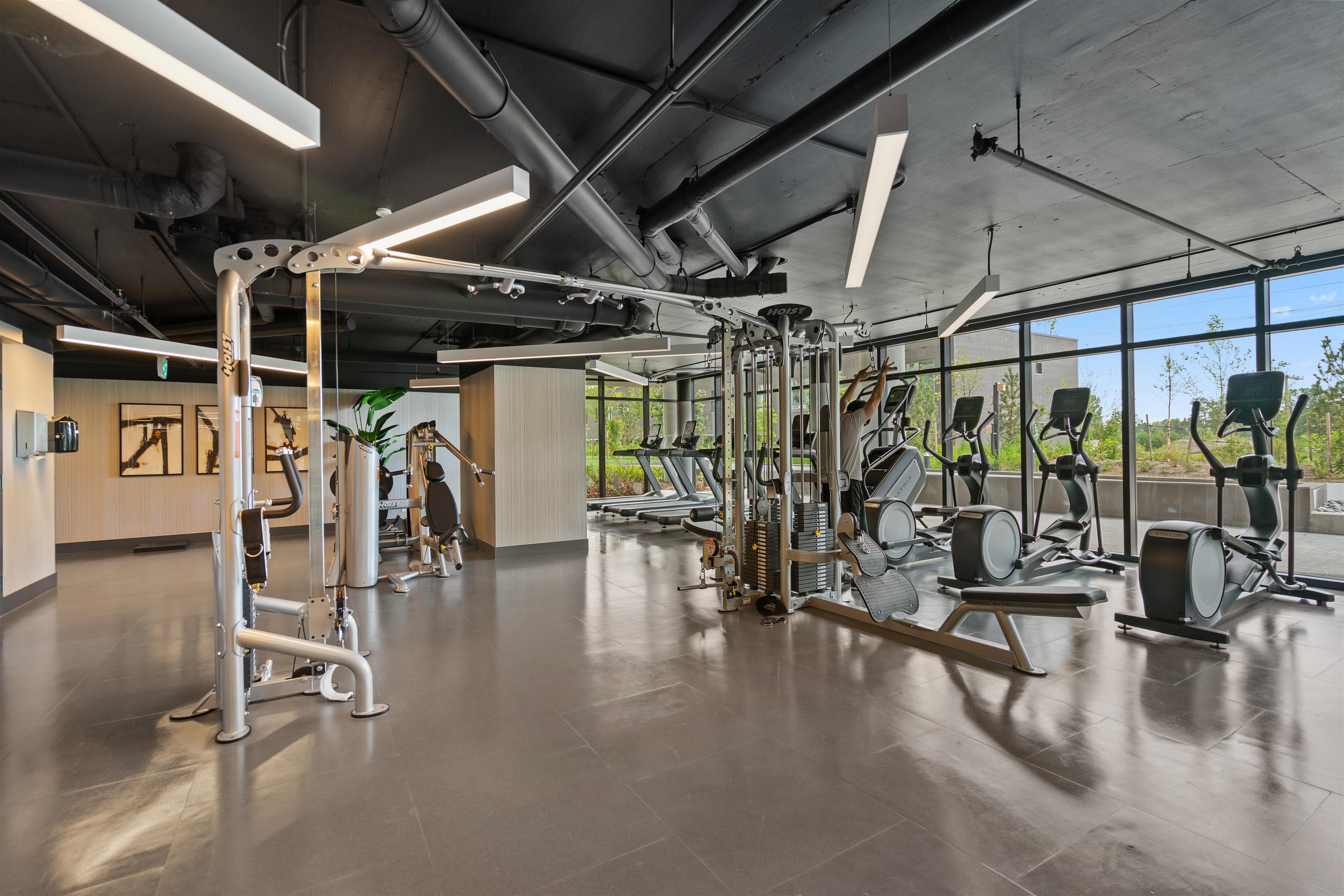 Fitness center with strength machines and cardio equipment beside large windows.