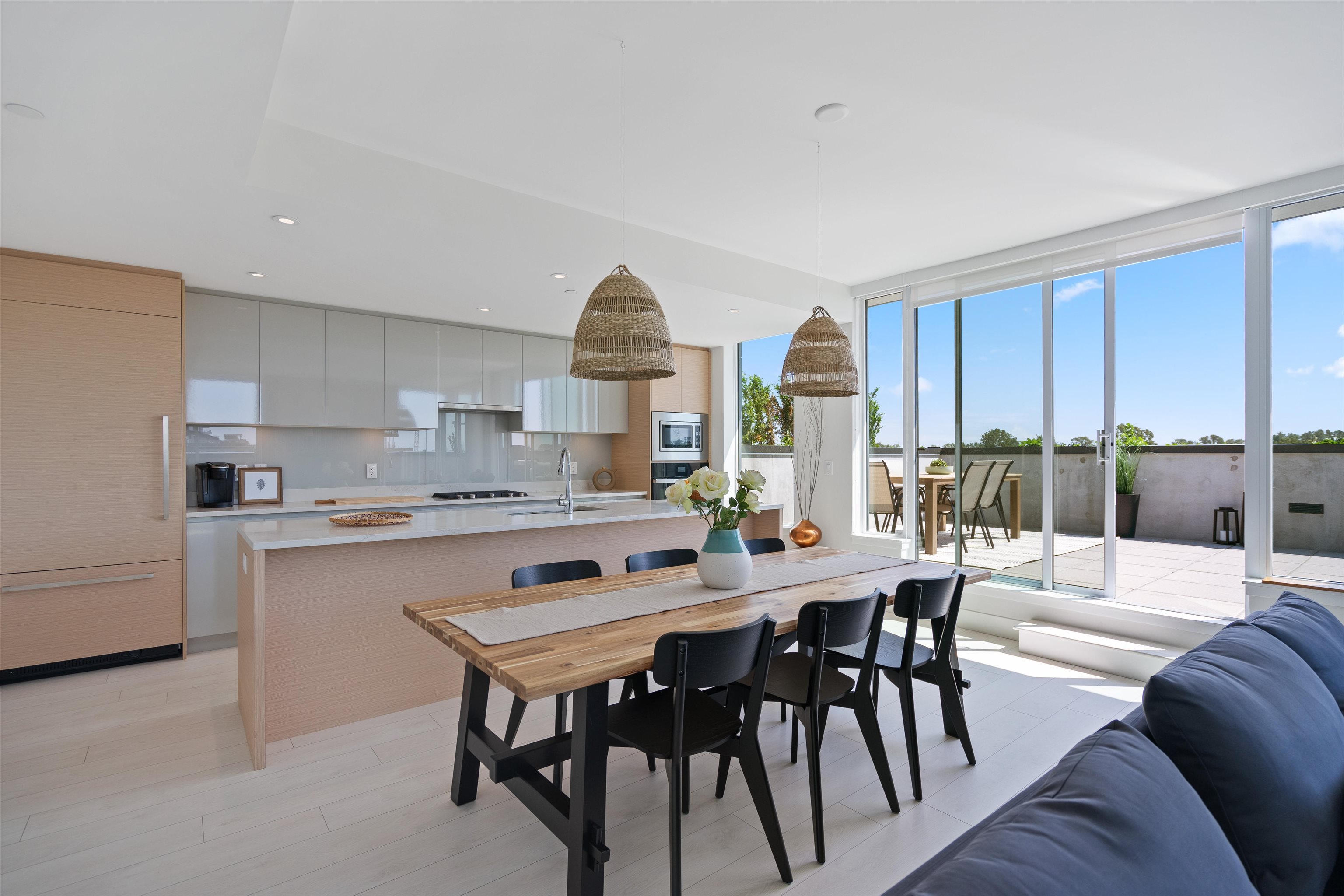 Open-plan kitchen and dining area with woven pendant lights and sliding doors to a sunny terrace.