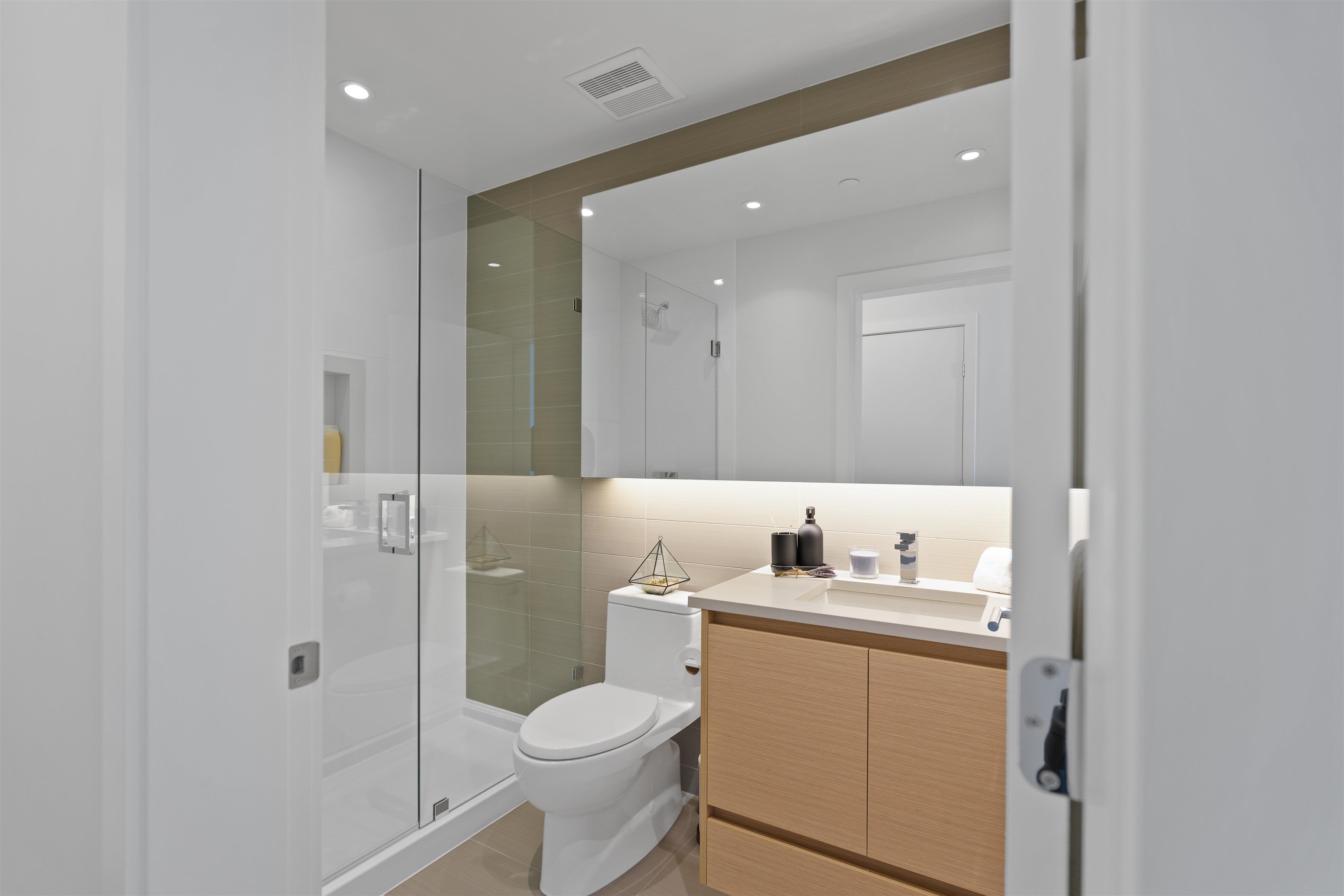 Modern bathroom with a glass shower, white toilet and light wood vanity.