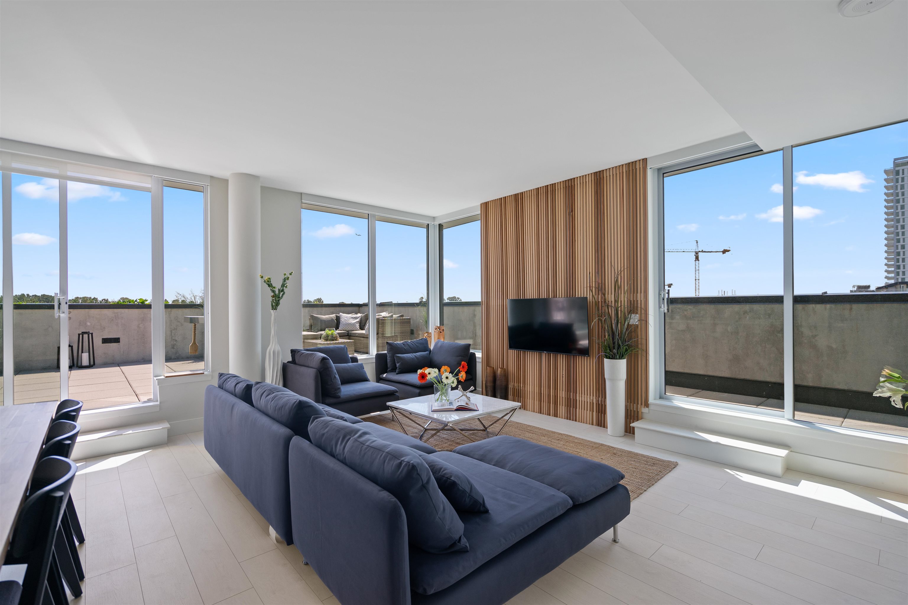 Bright living room with blue sectional sofas, a wood-slat TV wall, and floor-to-ceiling windows opening to a terrace.