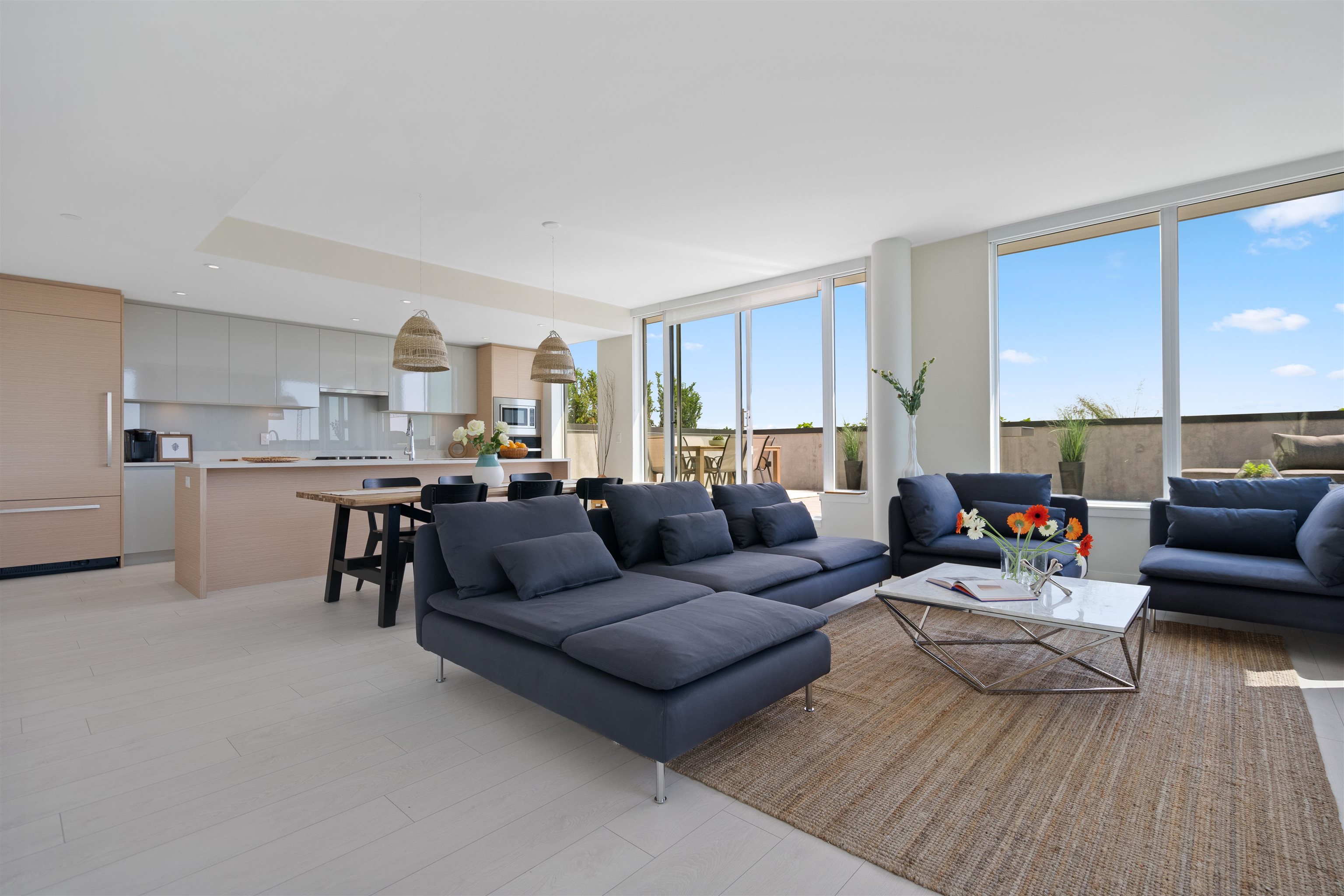 Open-plan living room with dark blue sectional sofas, a modern kitchen, and large windows overlooking a terrace.