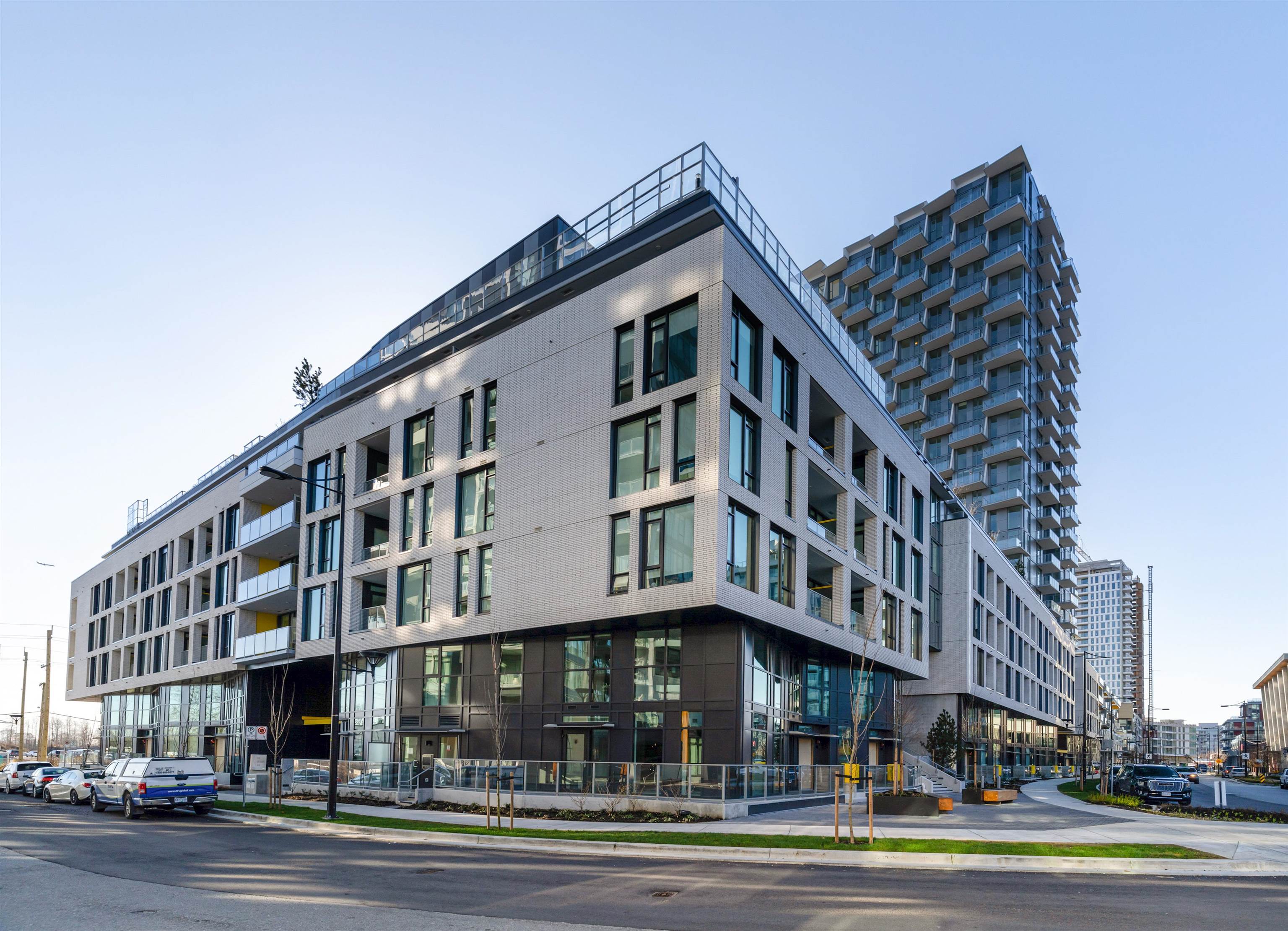 Modern light-brick condominium building with glass balconies and a taller residential tower behind it.