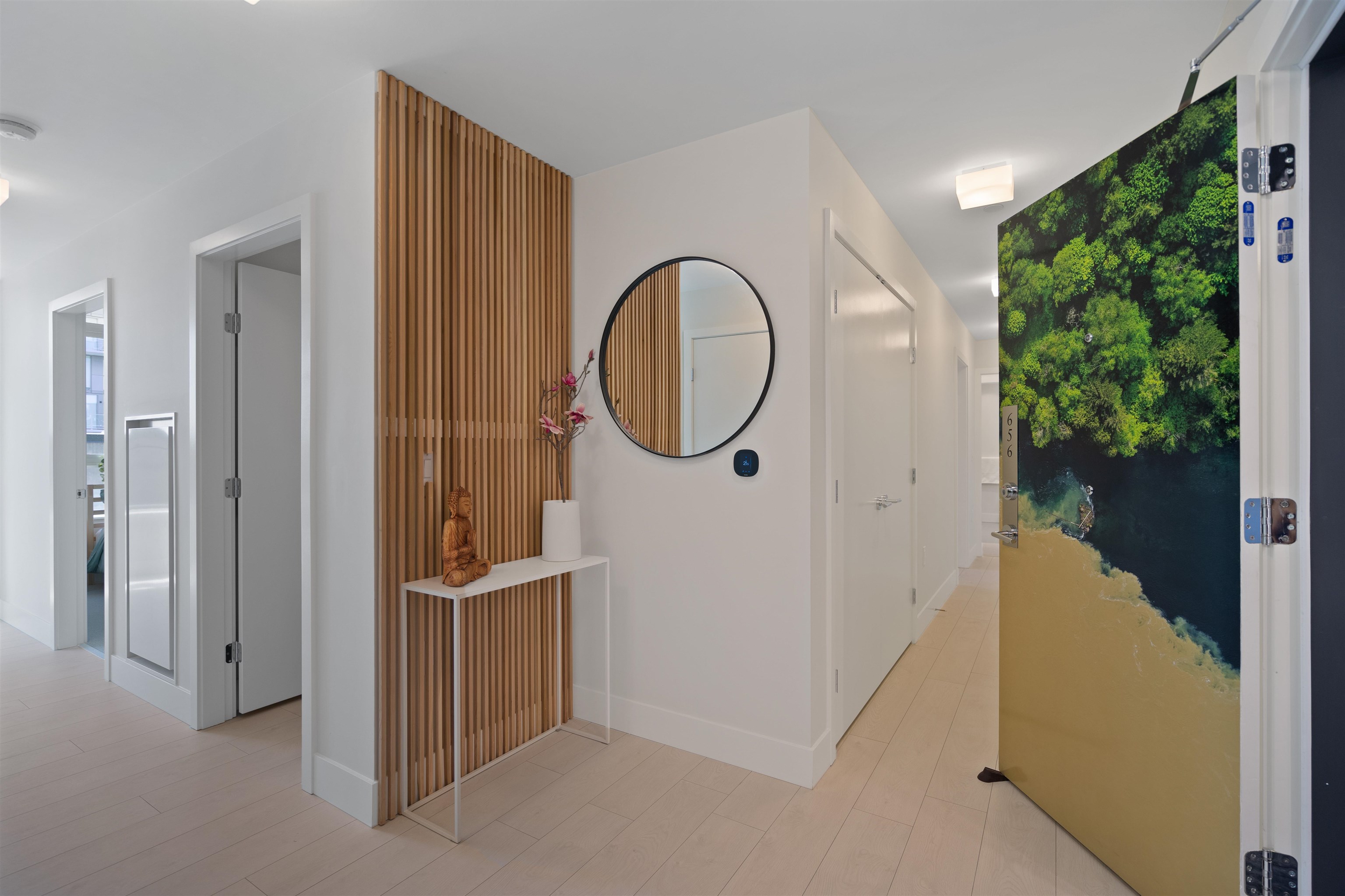 Condo entryway with a wood-slat accent wall, round mirror, and open door with a shoreline image.
