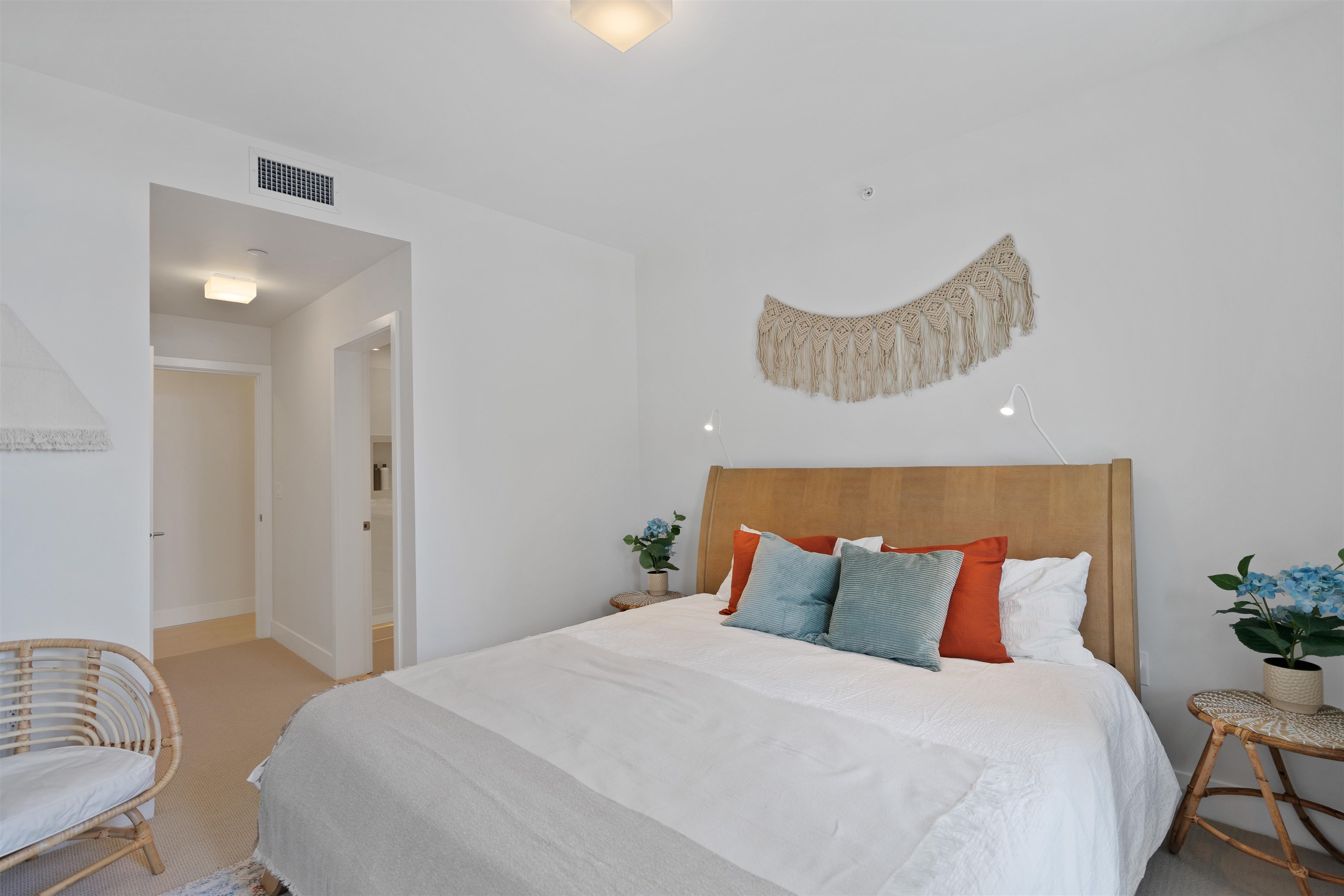 Bright bedroom with a wood headboard, colorful pillows, woven wall decor, and a rattan chair.