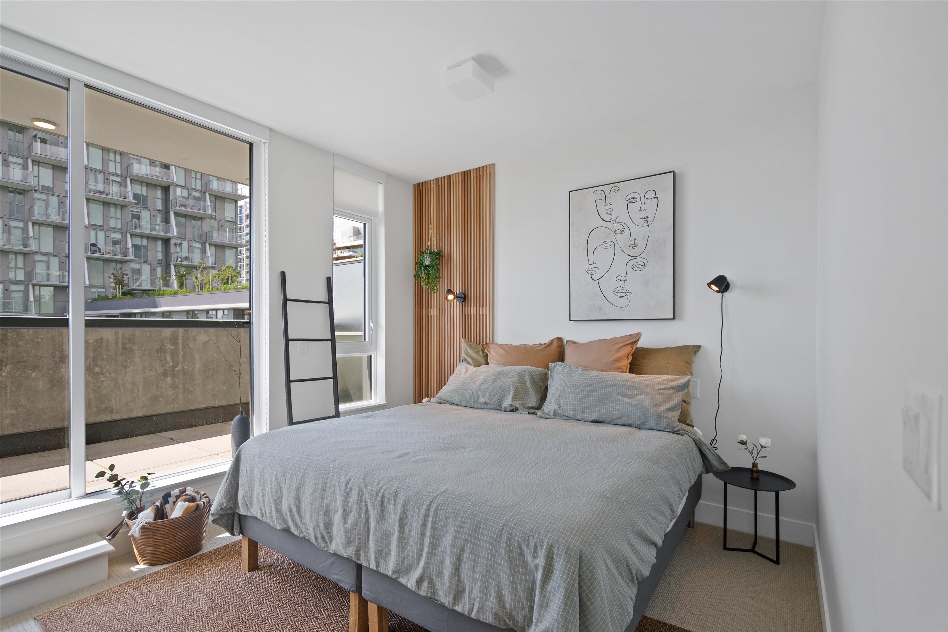 Staged condo bedroom with a large bed, wood-slat accent wall, and balcony windows overlooking neighboring apartments.