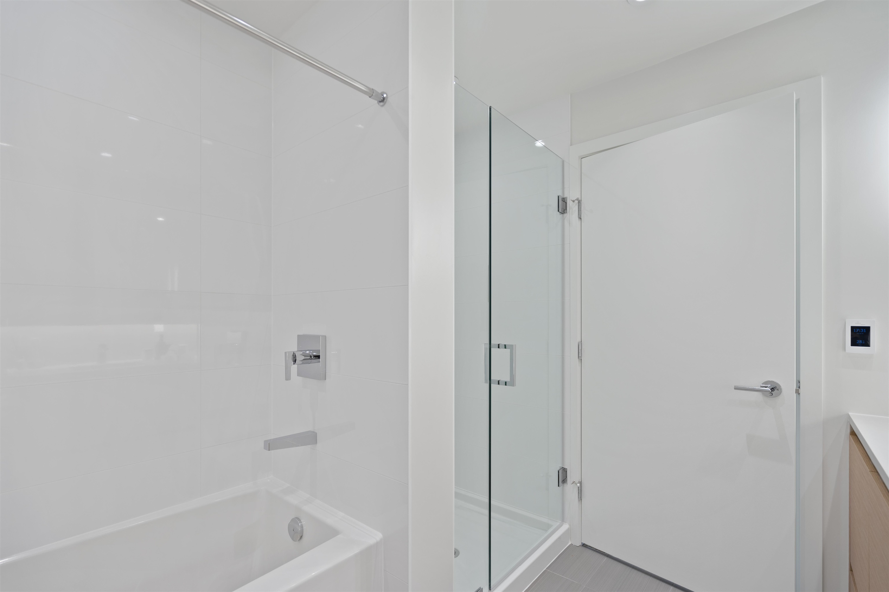 Modern bathroom with a white tiled bathtub, glass-enclosed shower, and chrome fixtures.