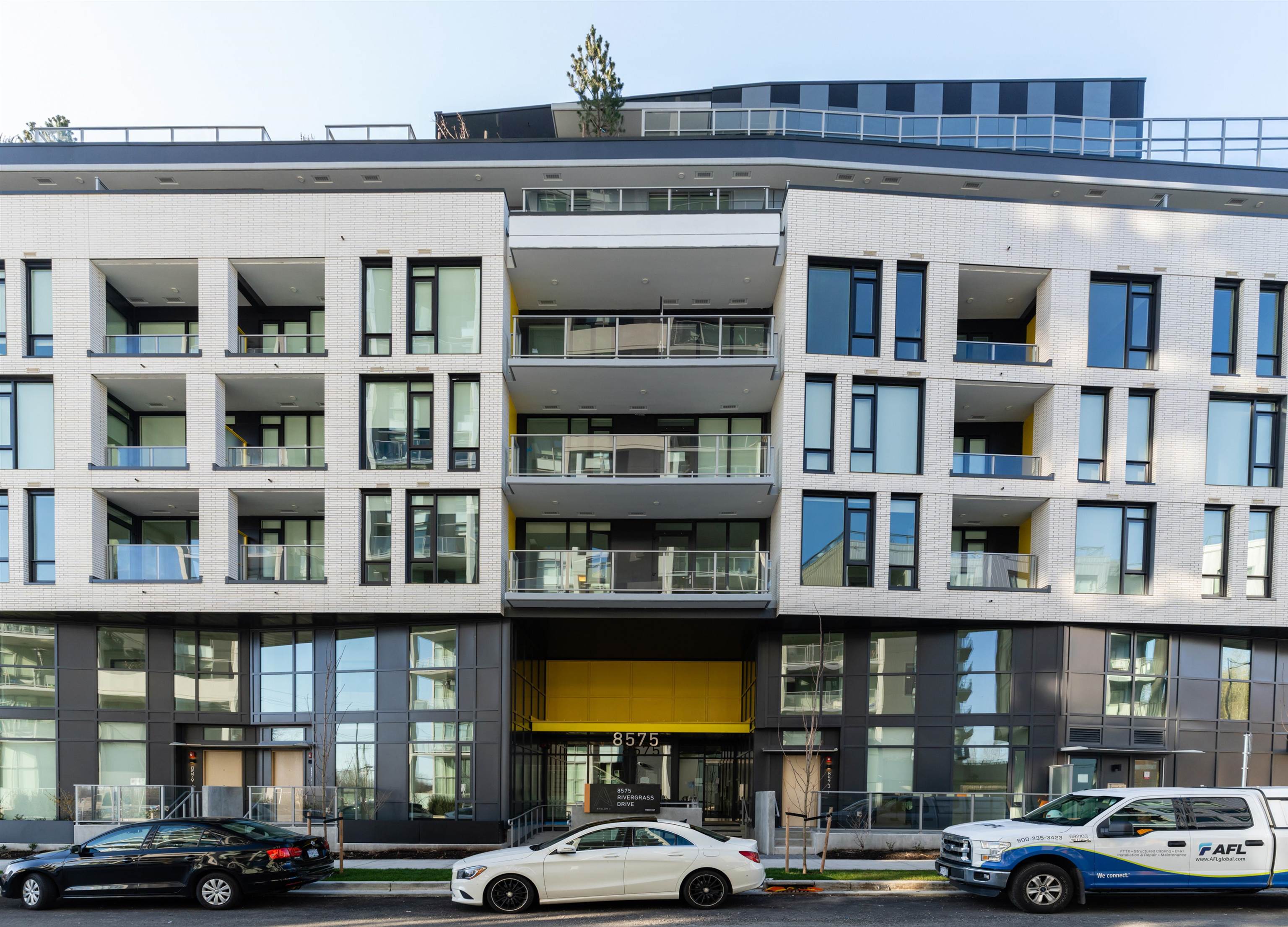 Modern apartment building with white brick, glass balconies, and a yellow entrance canopy.