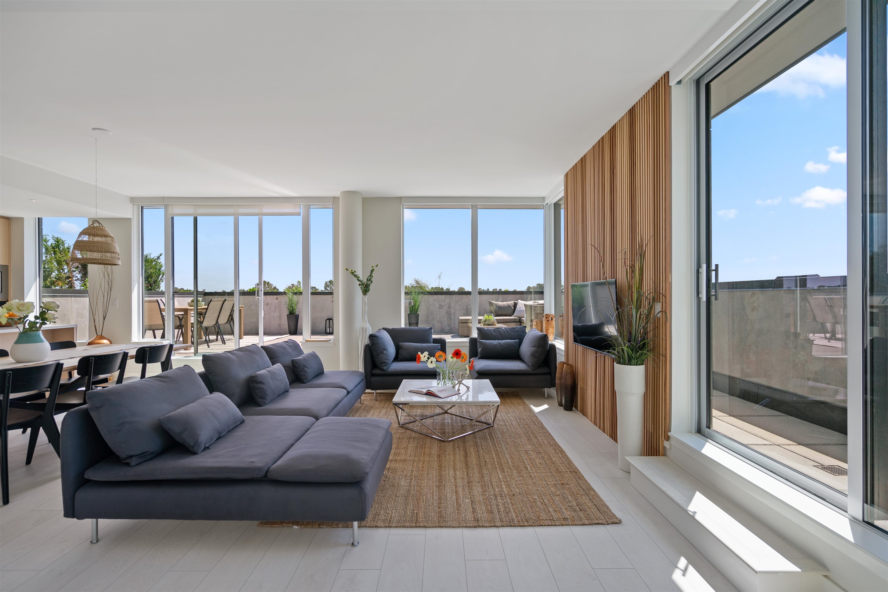 Living room with charcoal sectional, wood-slat wall, and expansive windows overlooking a terrace.