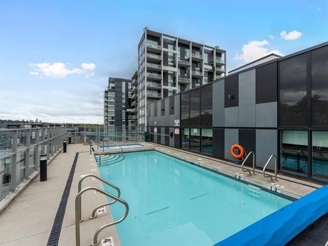 Rooftop condominium pool beside modern high-rise buildings, with glass railings and a wide concrete deck.