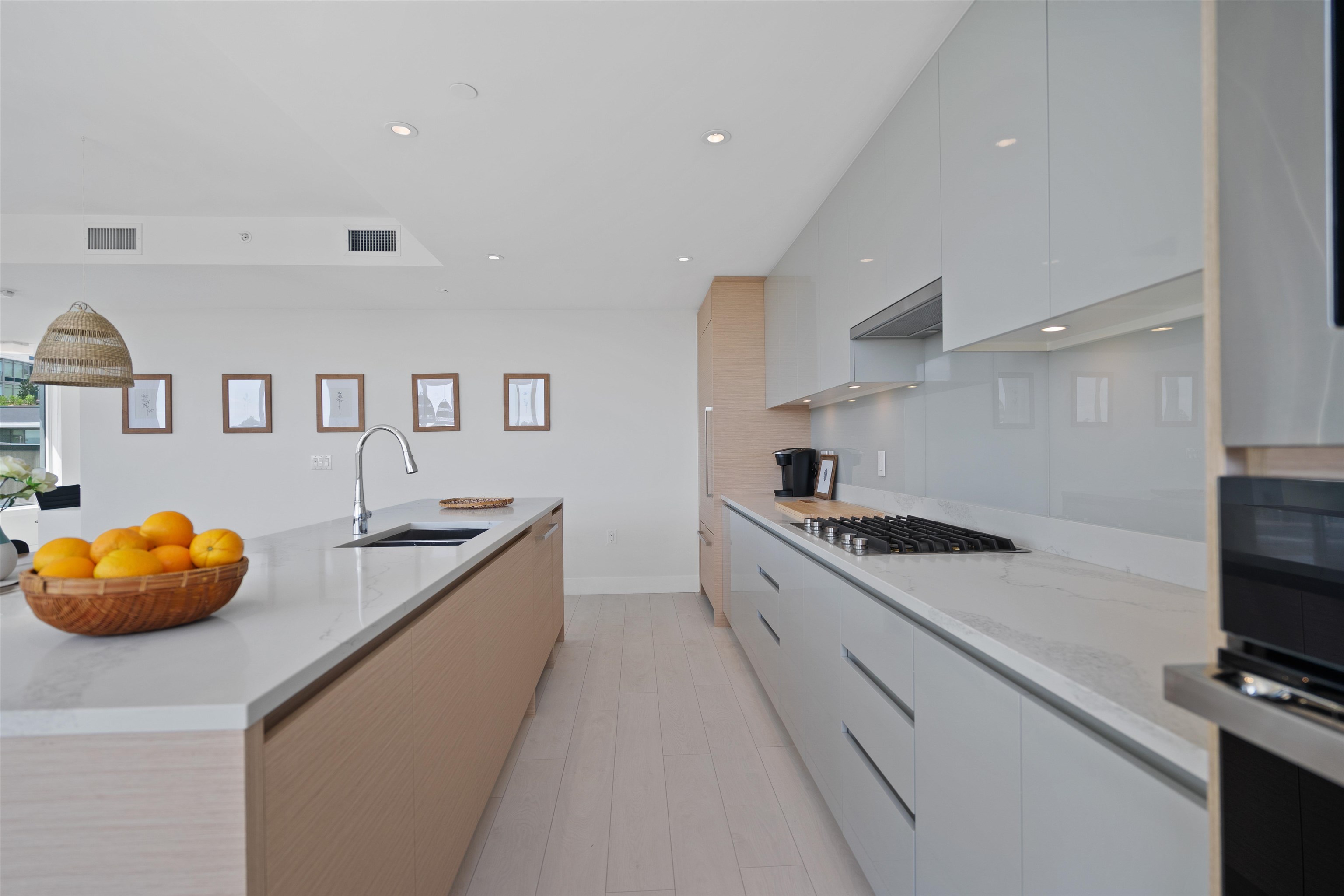 Modern kitchen with a wood-front island, white cabinetry, gas cooktop, and bowl of oranges.