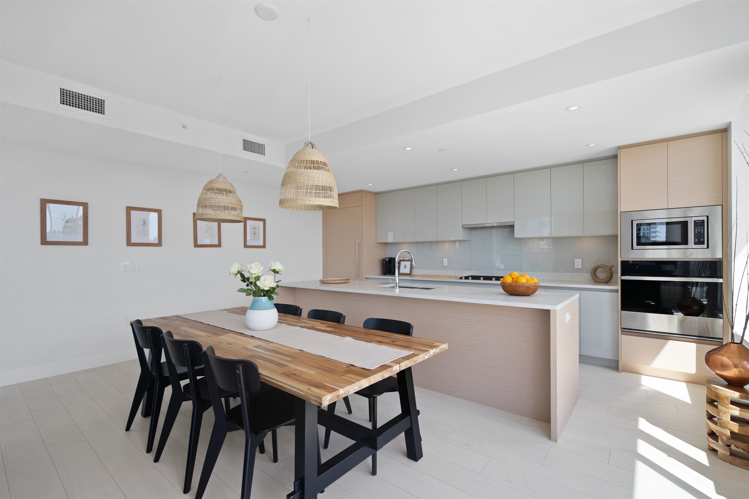 Open-plan kitchen and dining area with pale cabinetry, a large island, and a wood table beneath woven pendants.