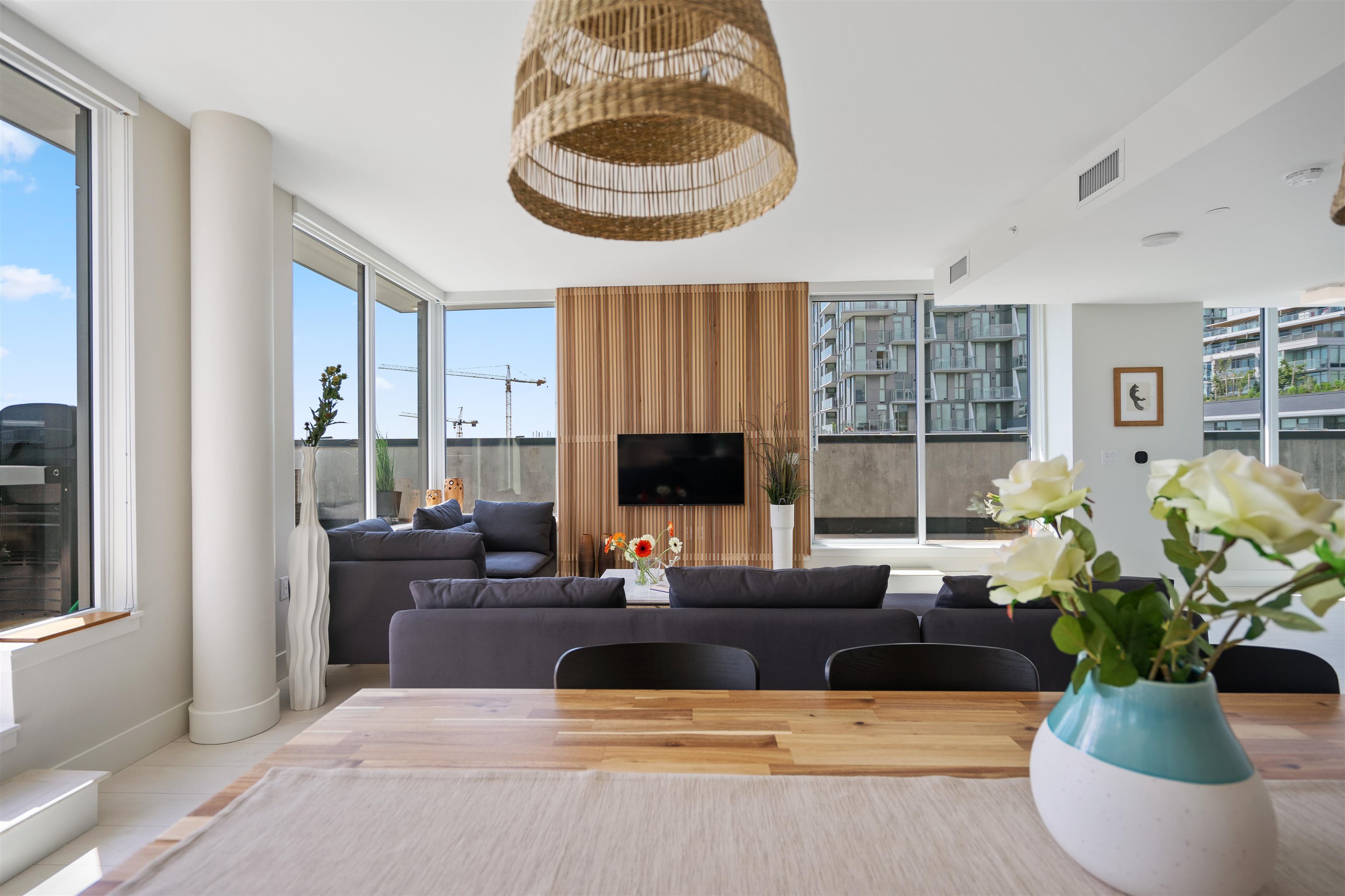 Bright condo living room with floor-to-ceiling windows, dark sectional seating, and a wood-slat TV wall.