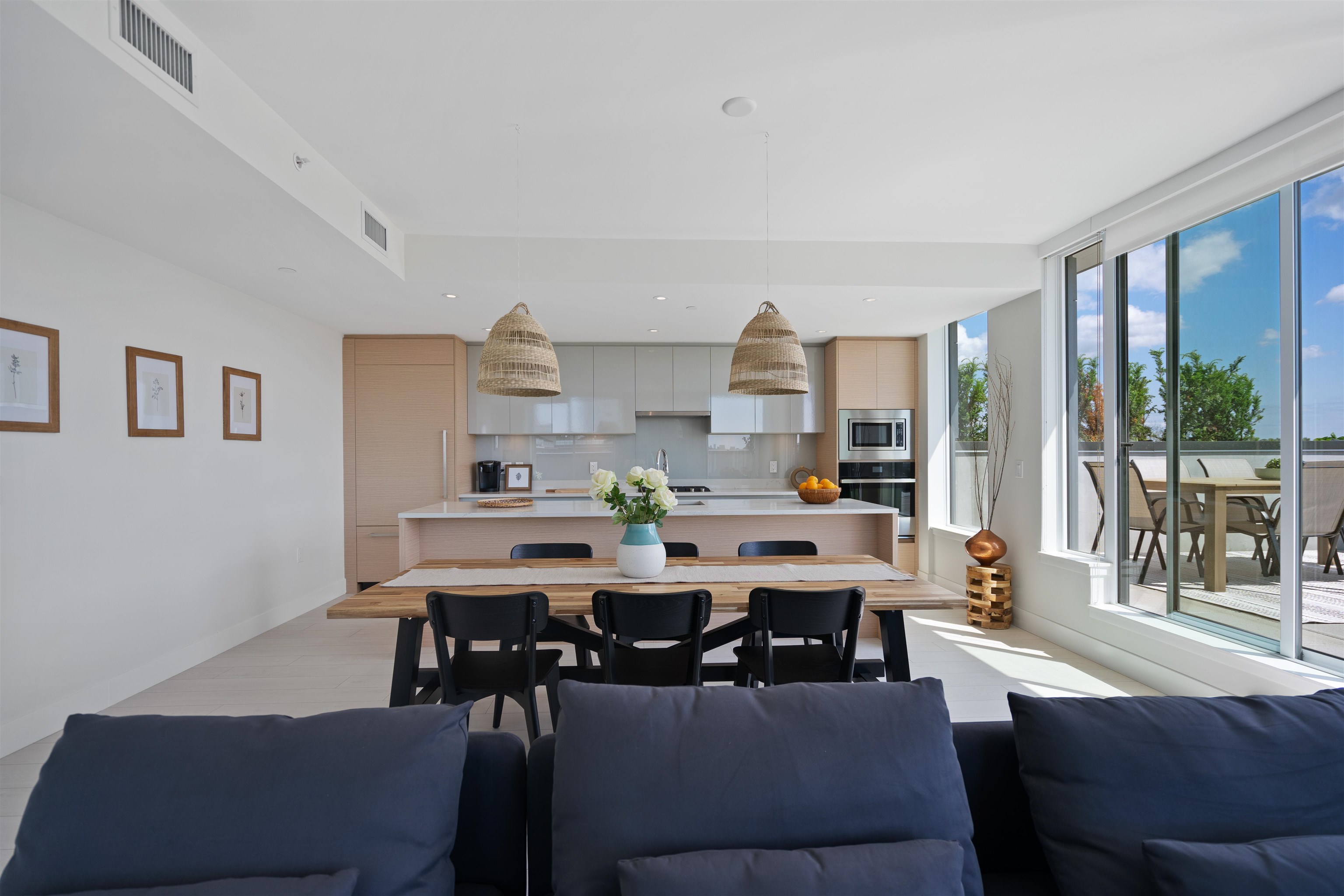 Open-plan kitchen and dining area with a wood island, woven pendant lights, and windows overlooking a balcony.