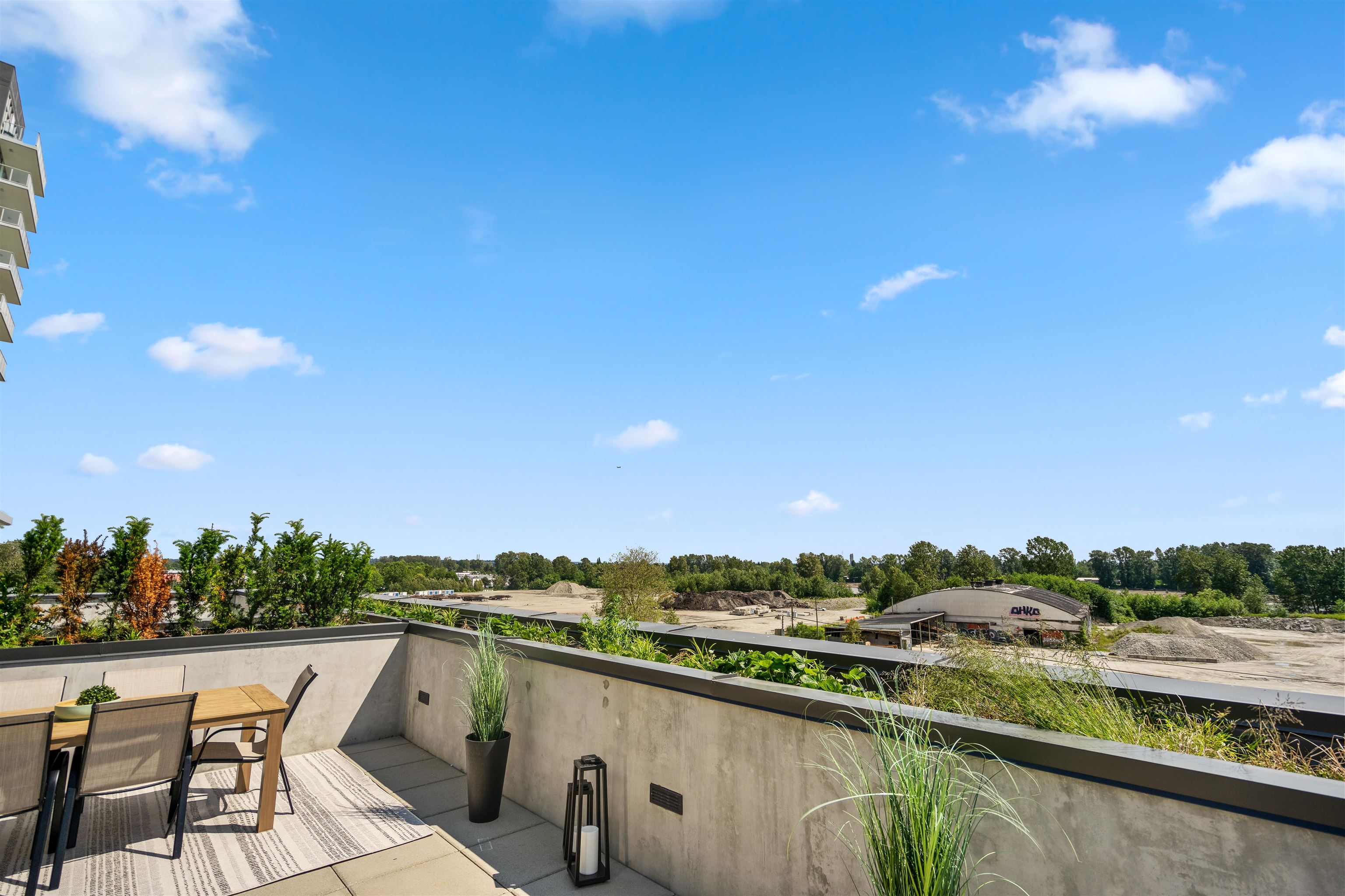 Outdoor terrace with dining furniture and potted grasses overlooking trees and a construction area.