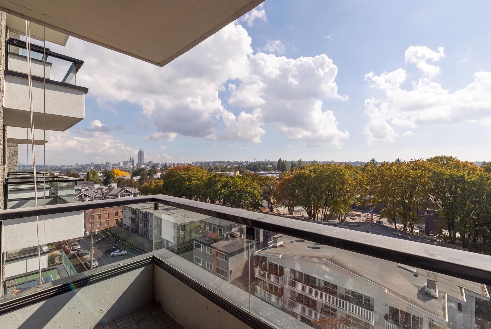 Apartment balcony overlooking autumn trees, rooftops, and a distant city skyline.
