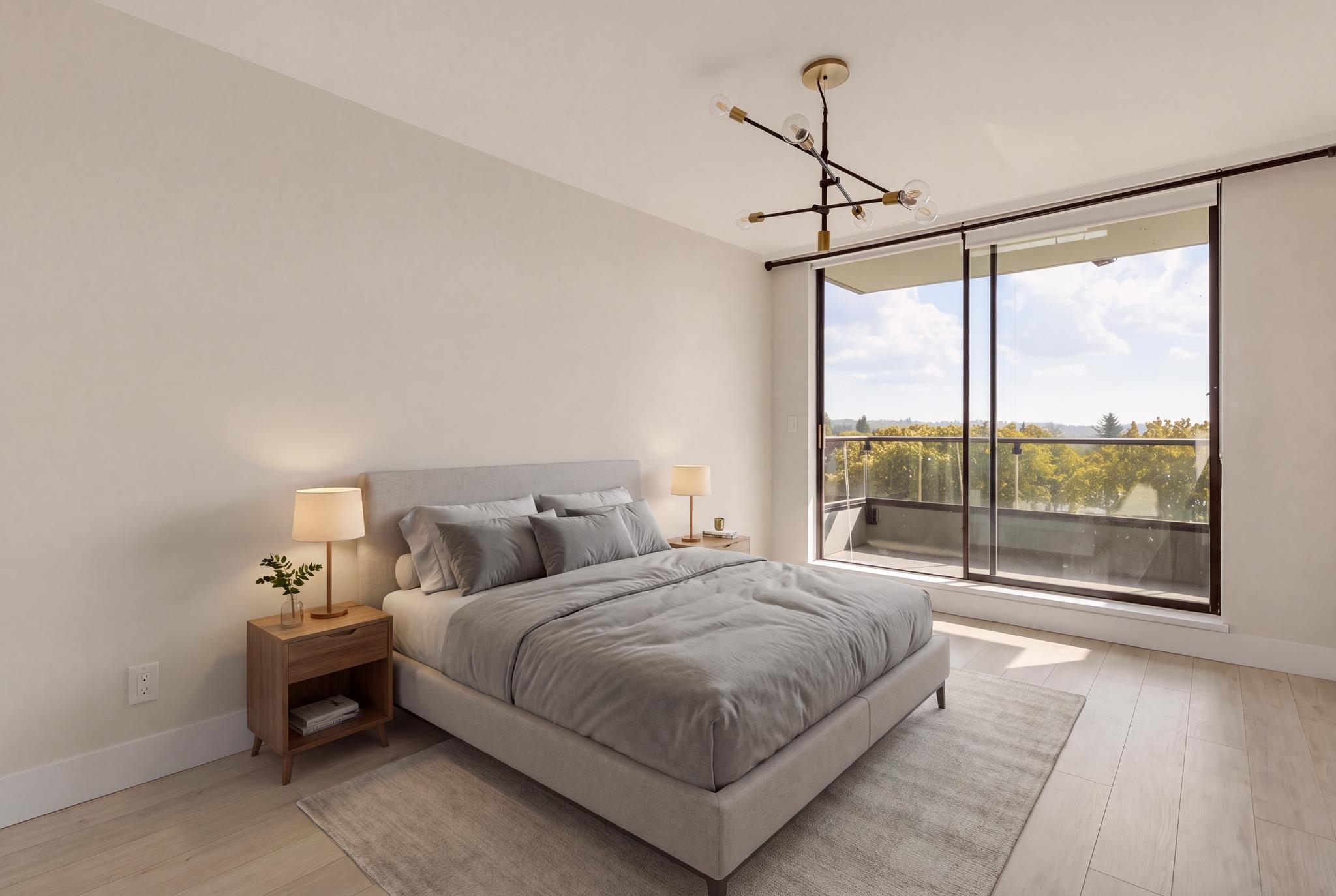 Staged bedroom with a gray bed and floor-to-ceiling balcony doors overlooking treetops.
