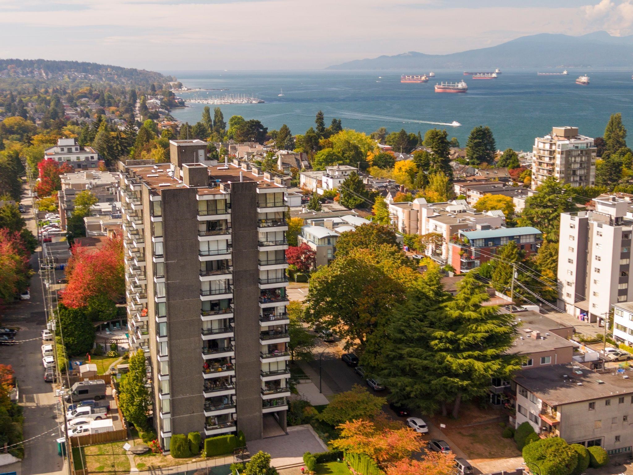 Residential tower overlooking Vancouver Harbour, with cargo ships, a marina, and autumn-colored trees.