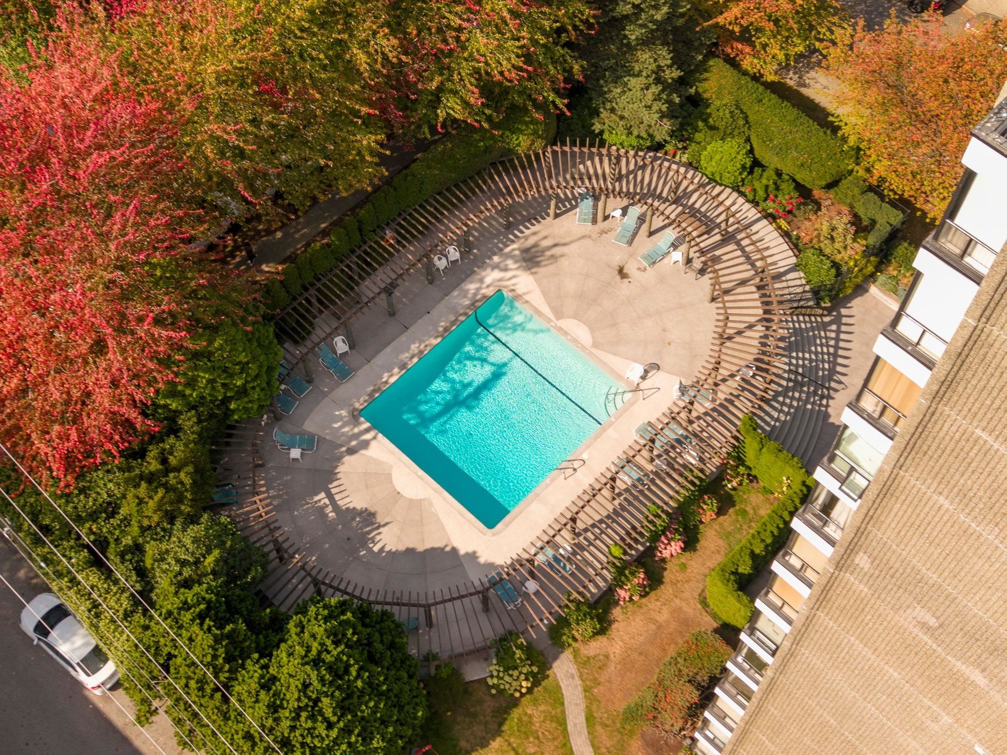 Outdoor pool in a landscaped condominium courtyard, surrounded by a curved pergola and autumn foliage.