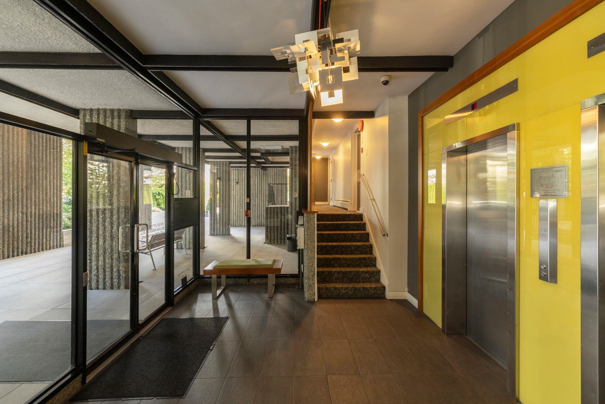 Building lobby with stainless-steel elevators, carpeted stairs, and glass entrance doors.