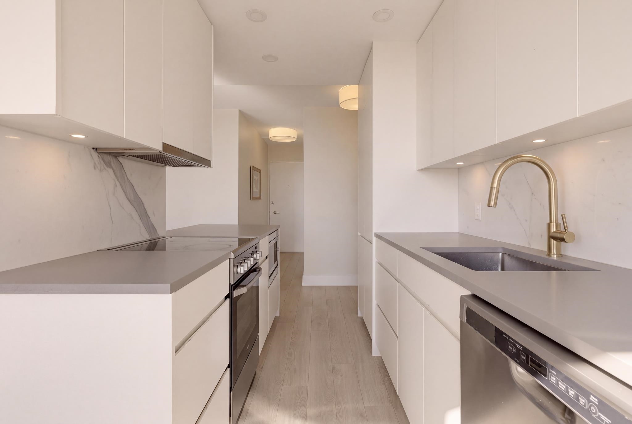 Modern condo kitchen with white cabinetry, marble backsplash, brass faucet, and integrated appliances.