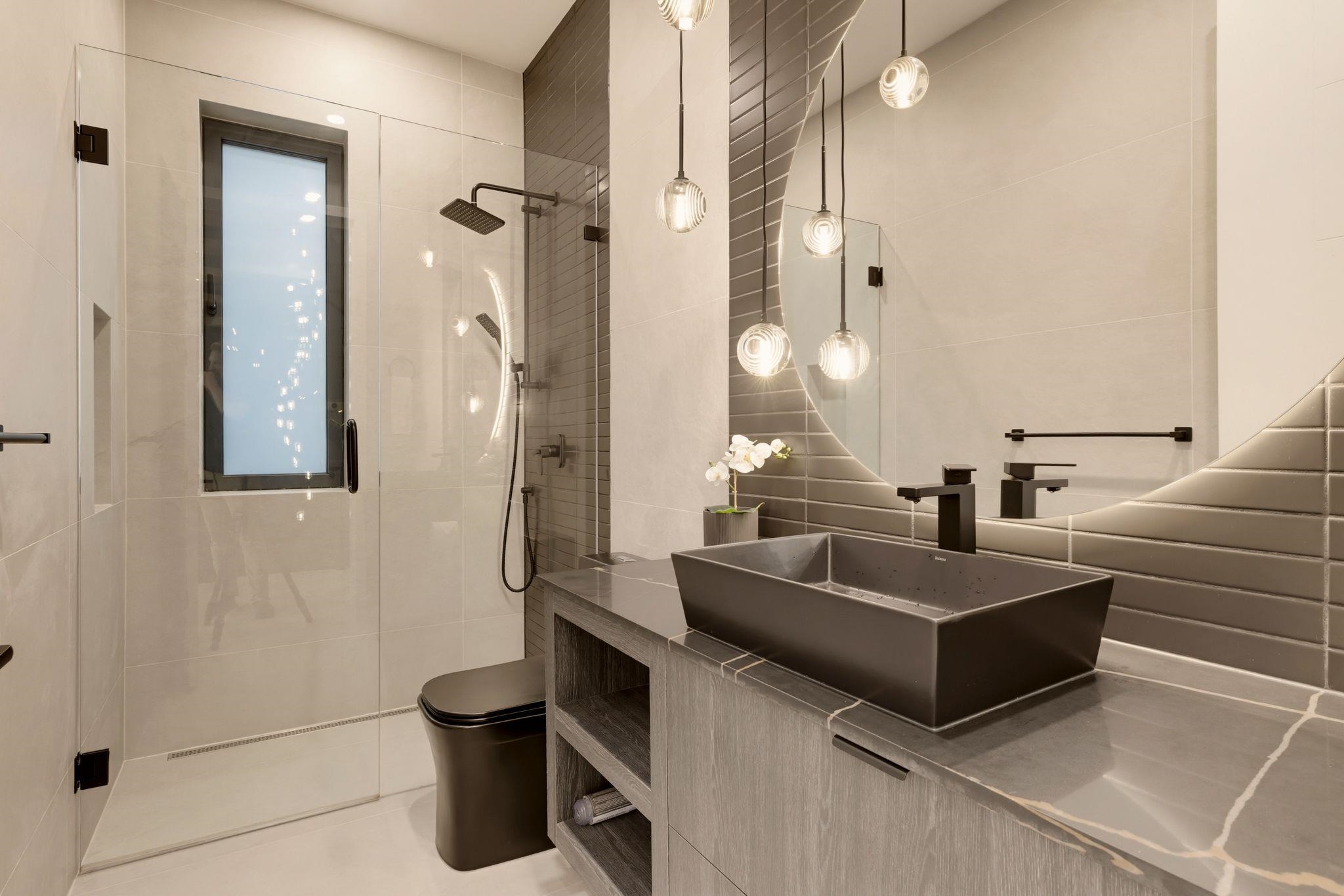 Modern bathroom with glass shower, dark vessel sink, and glowing globe pendant lights.