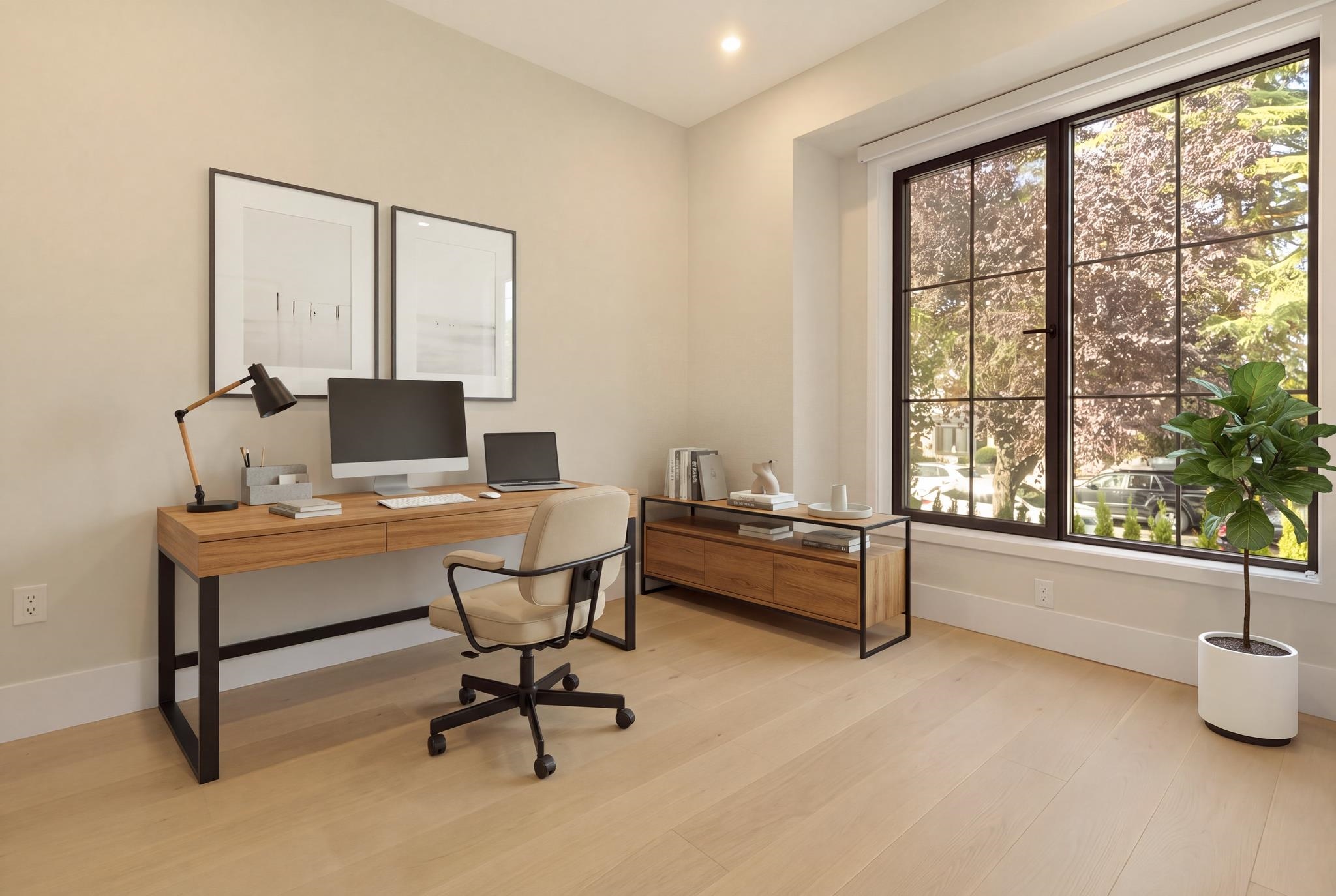 Staged home office with a wood desk and computer beside a large window overlooking leafy trees.