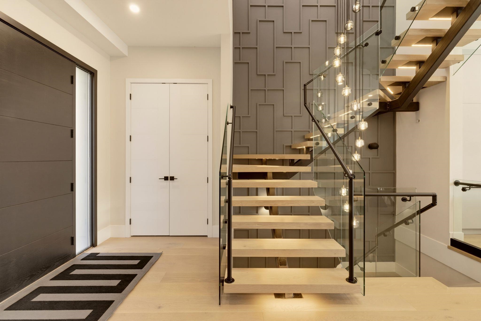 Entry foyer with a floating wood staircase, glass railings, and a geometric gray feature wall.