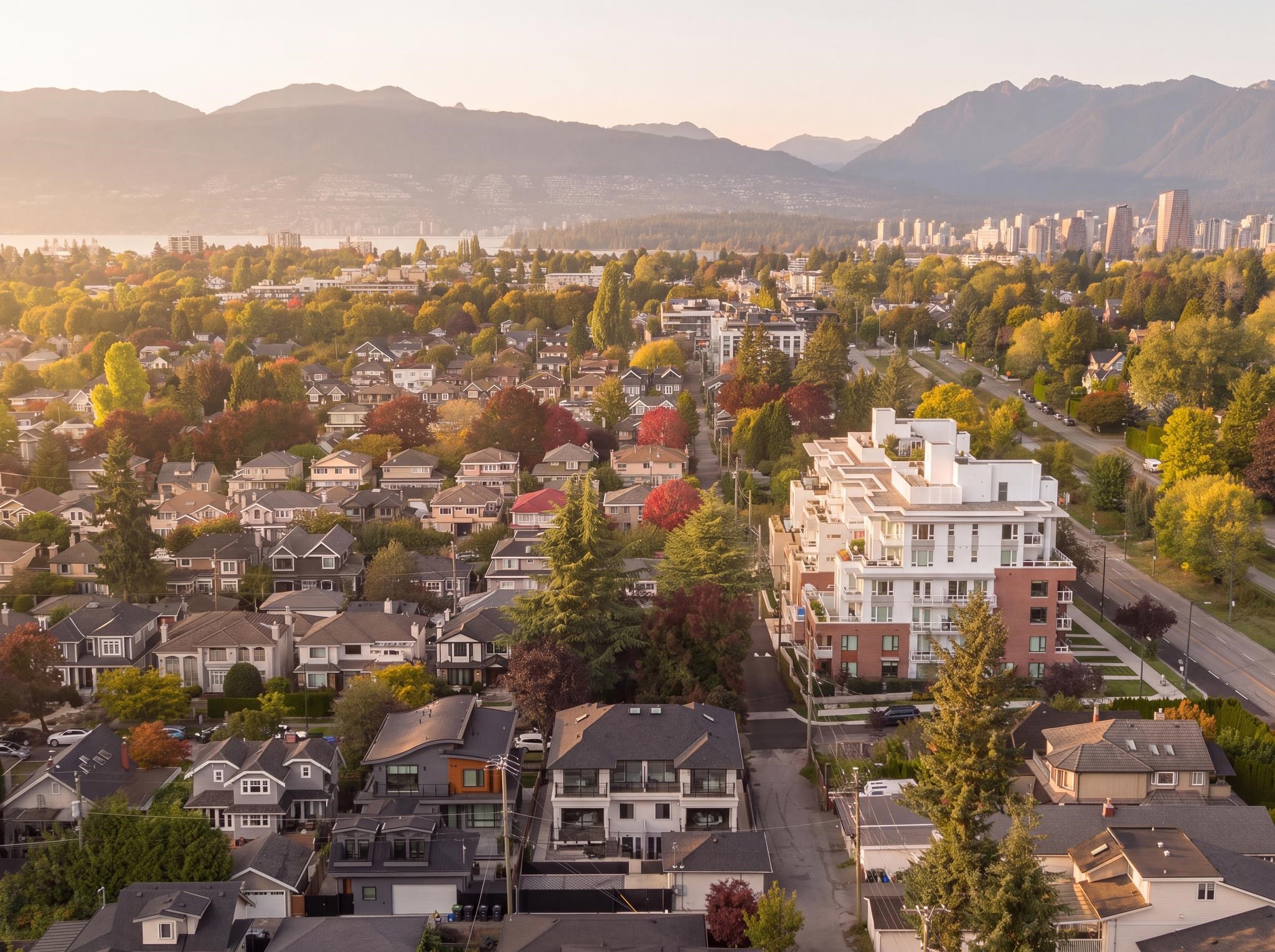 Aerial view of a Vancouver neighborhood with autumn trees, downtown towers, water, and mountains beyond.