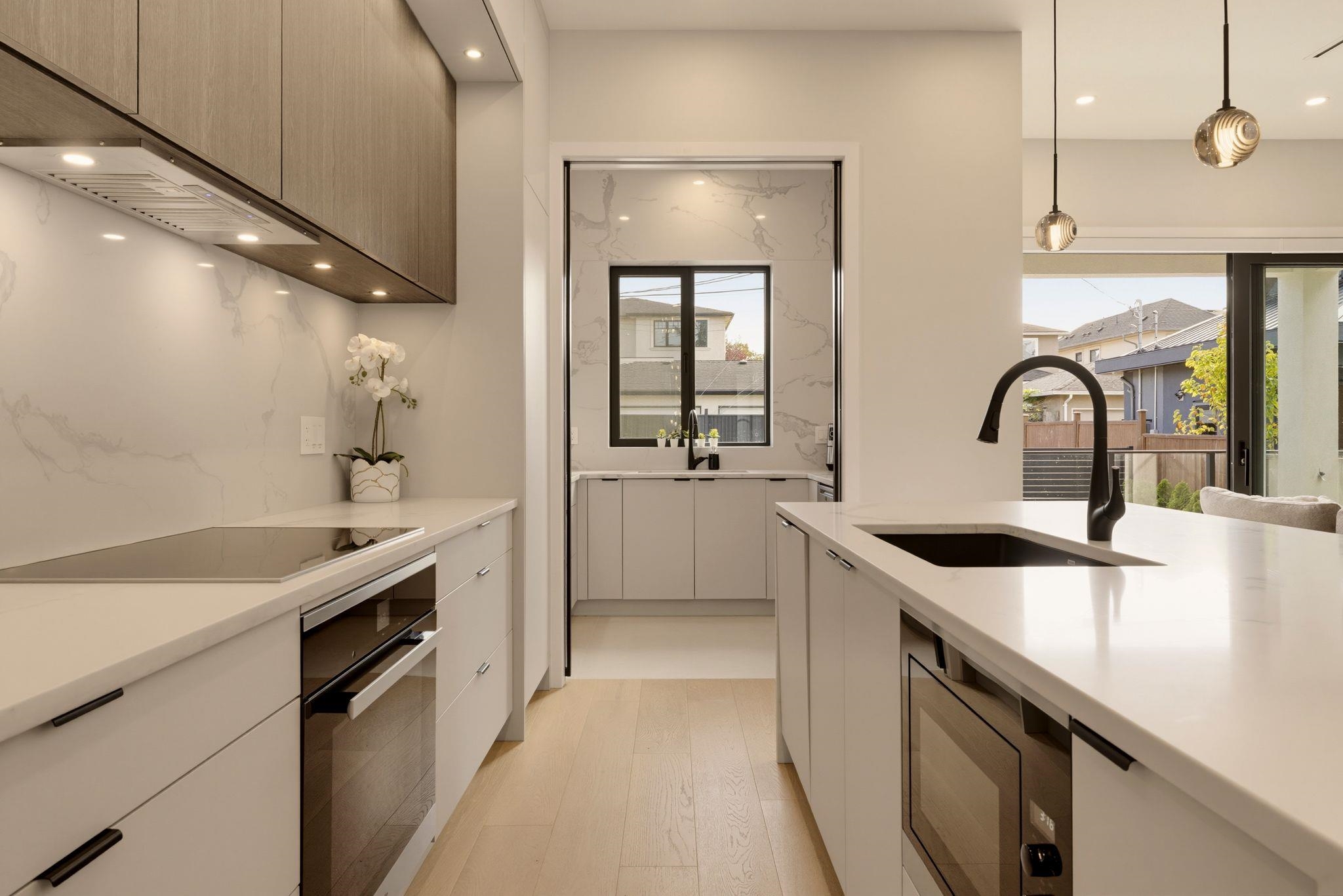 Modern kitchen with a veined stone backsplash, pale wood cabinets, and a large island sink.