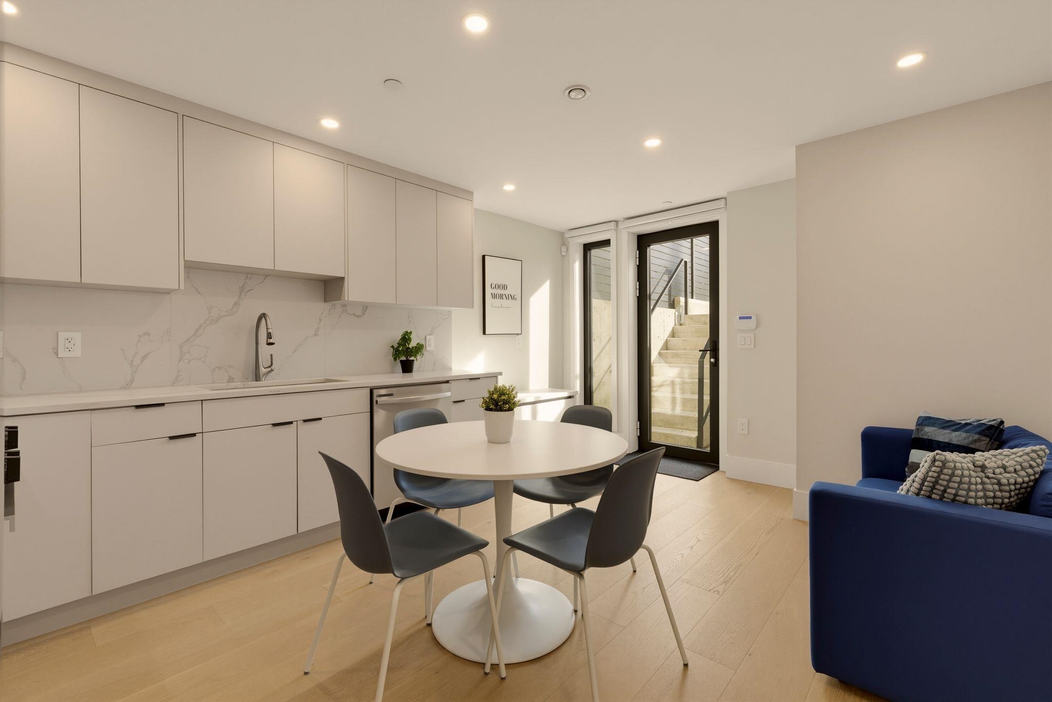 Furnished kitchen and dining area with white cabinets, round table, and glass door to exterior steps.
