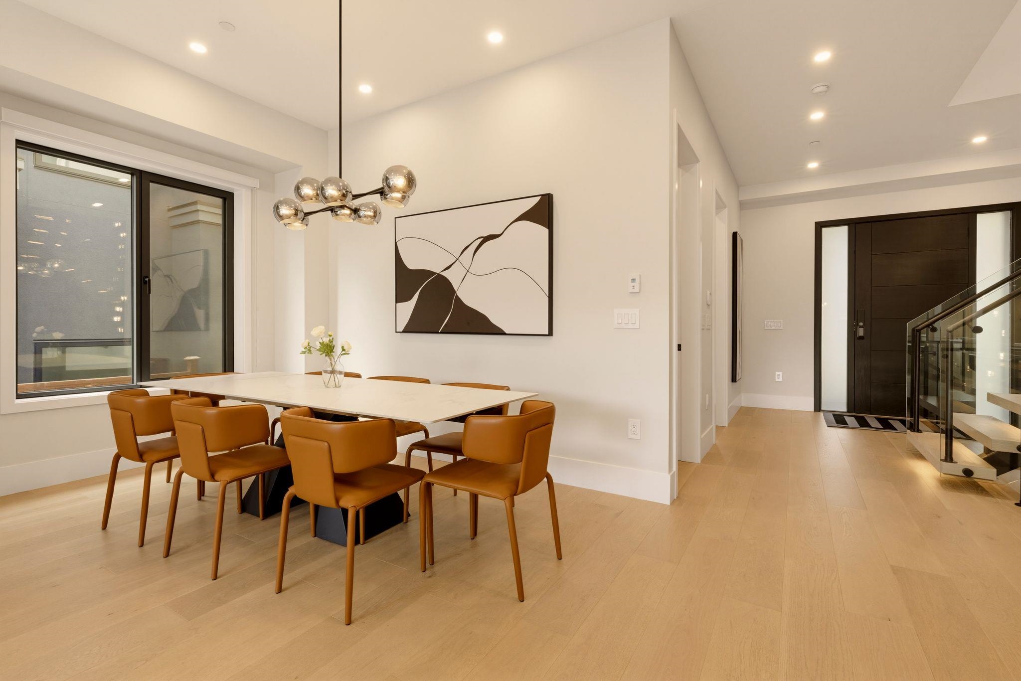 Modern dining room with caramel leather chairs, a white table, and a sculptural pendant light.